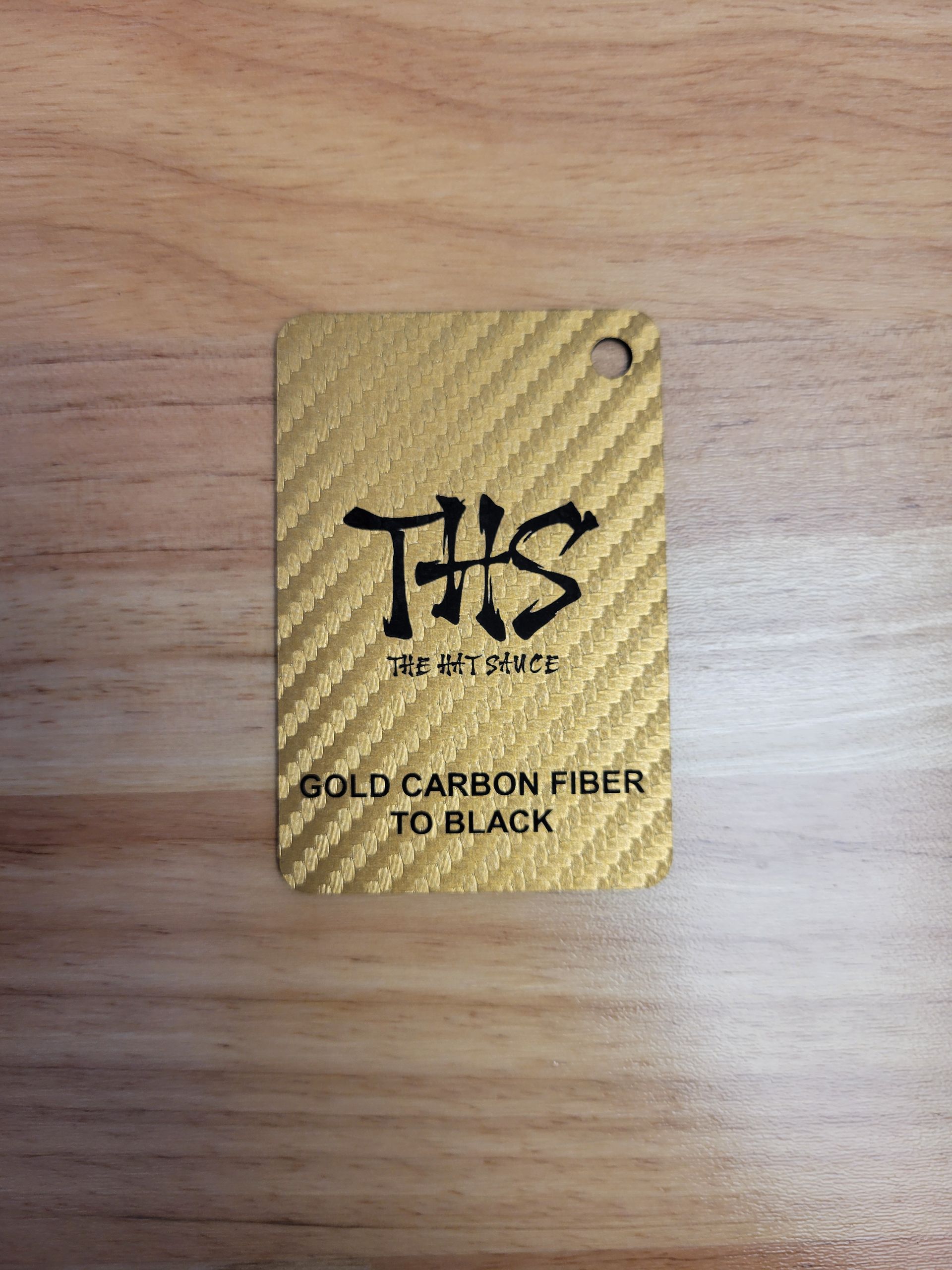 A gold carbon fiber tag is sitting on a wooden table.