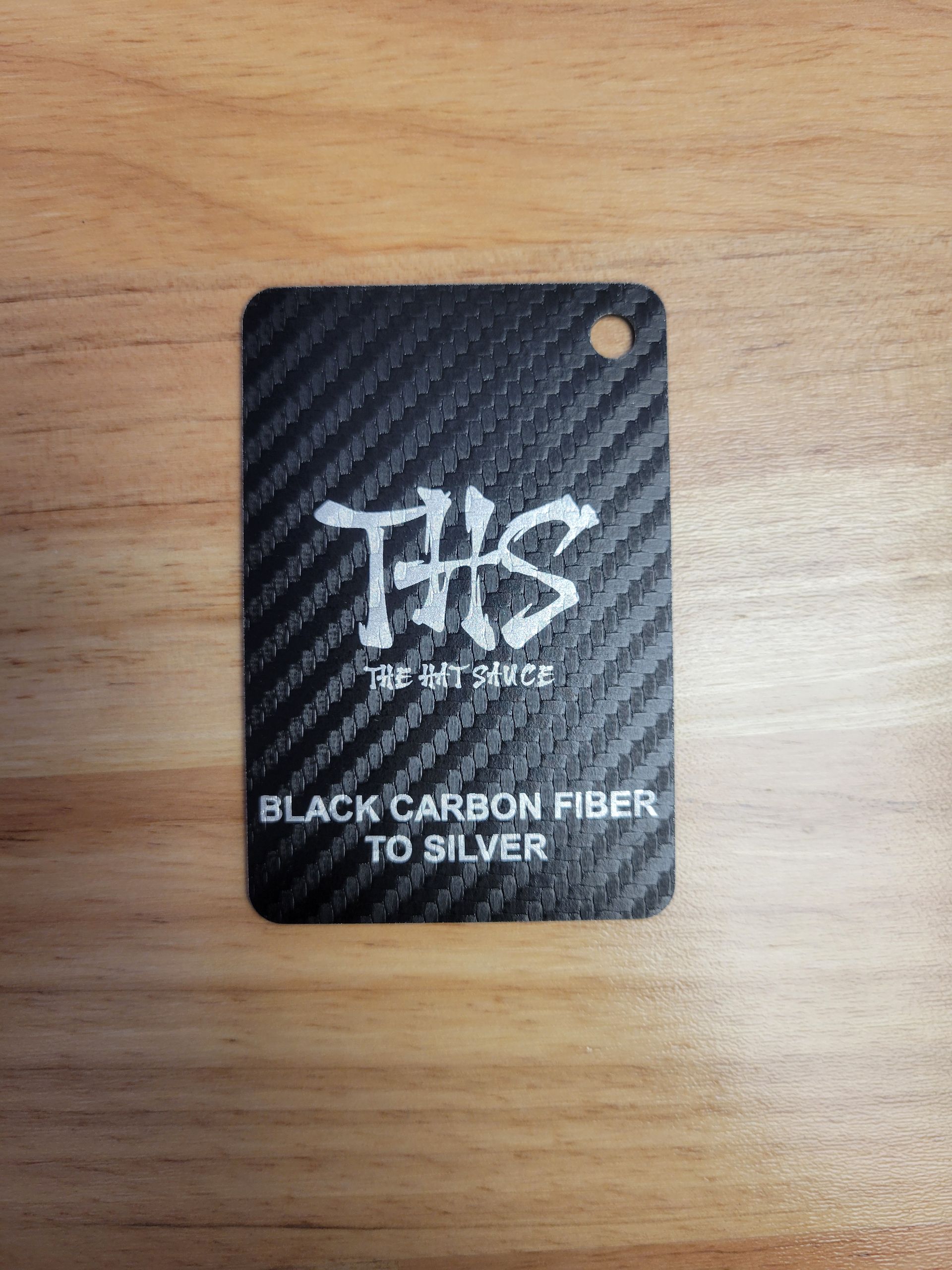 A black carbon fiber tag is sitting on a wooden table.