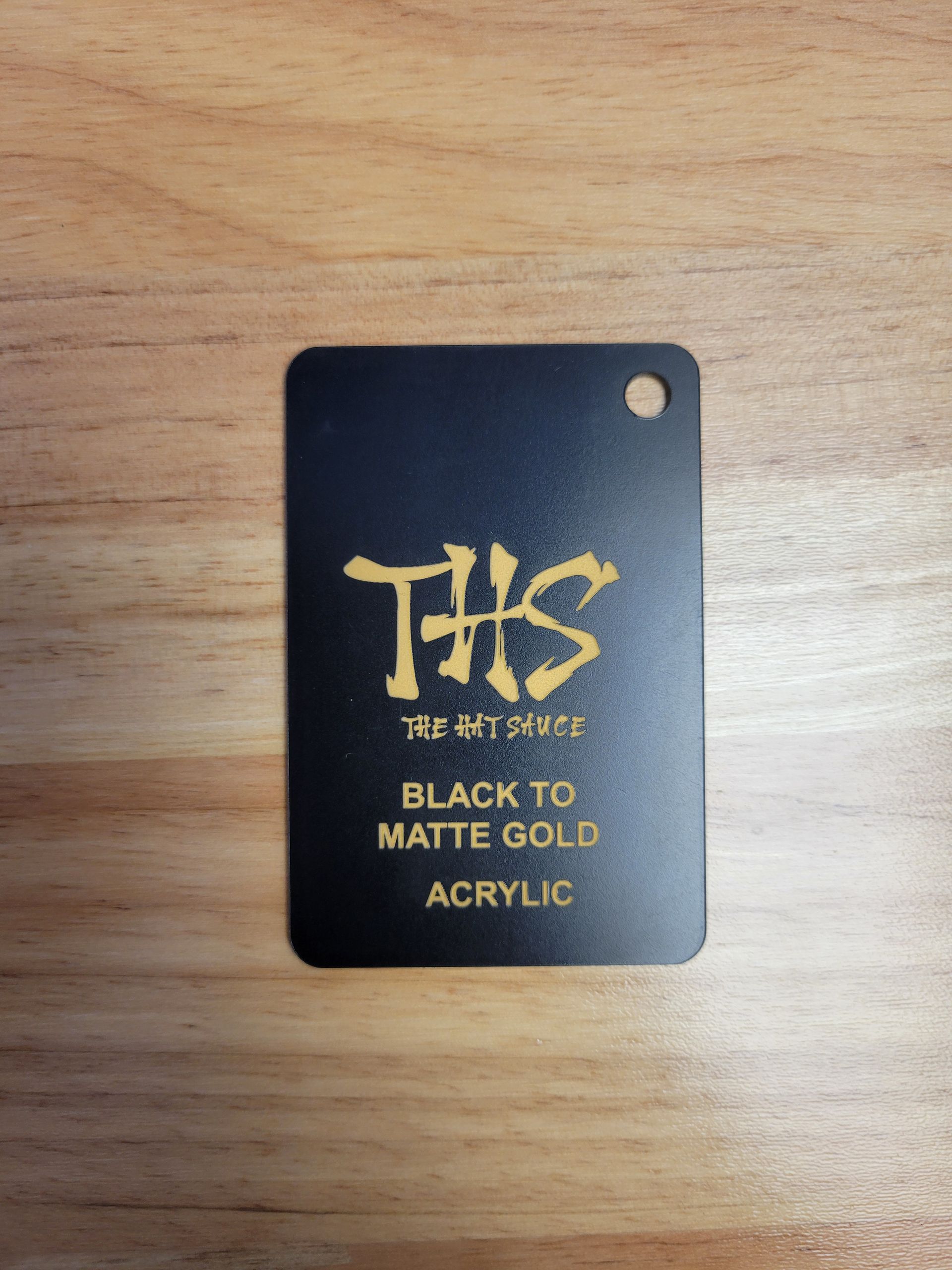 A black to matte gold acrylic tag on a wooden table