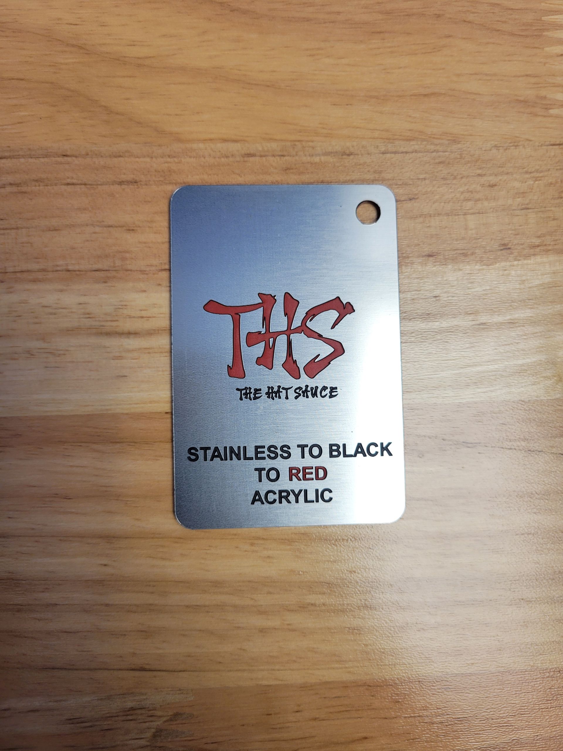 A stainless to black to red acrylic tag is sitting on a wooden table.