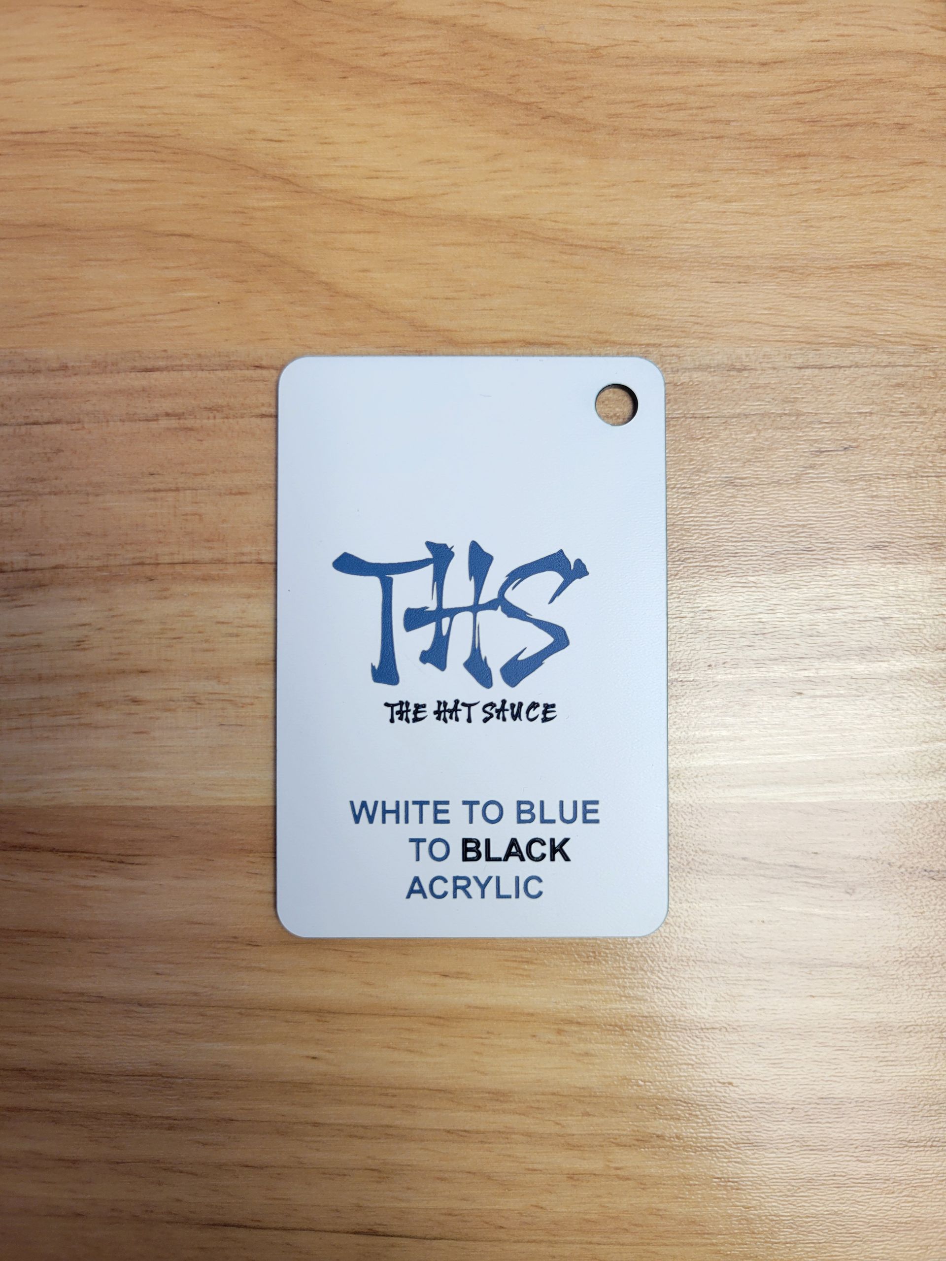 A white to blue to black acrylic tag is sitting on a wooden table.