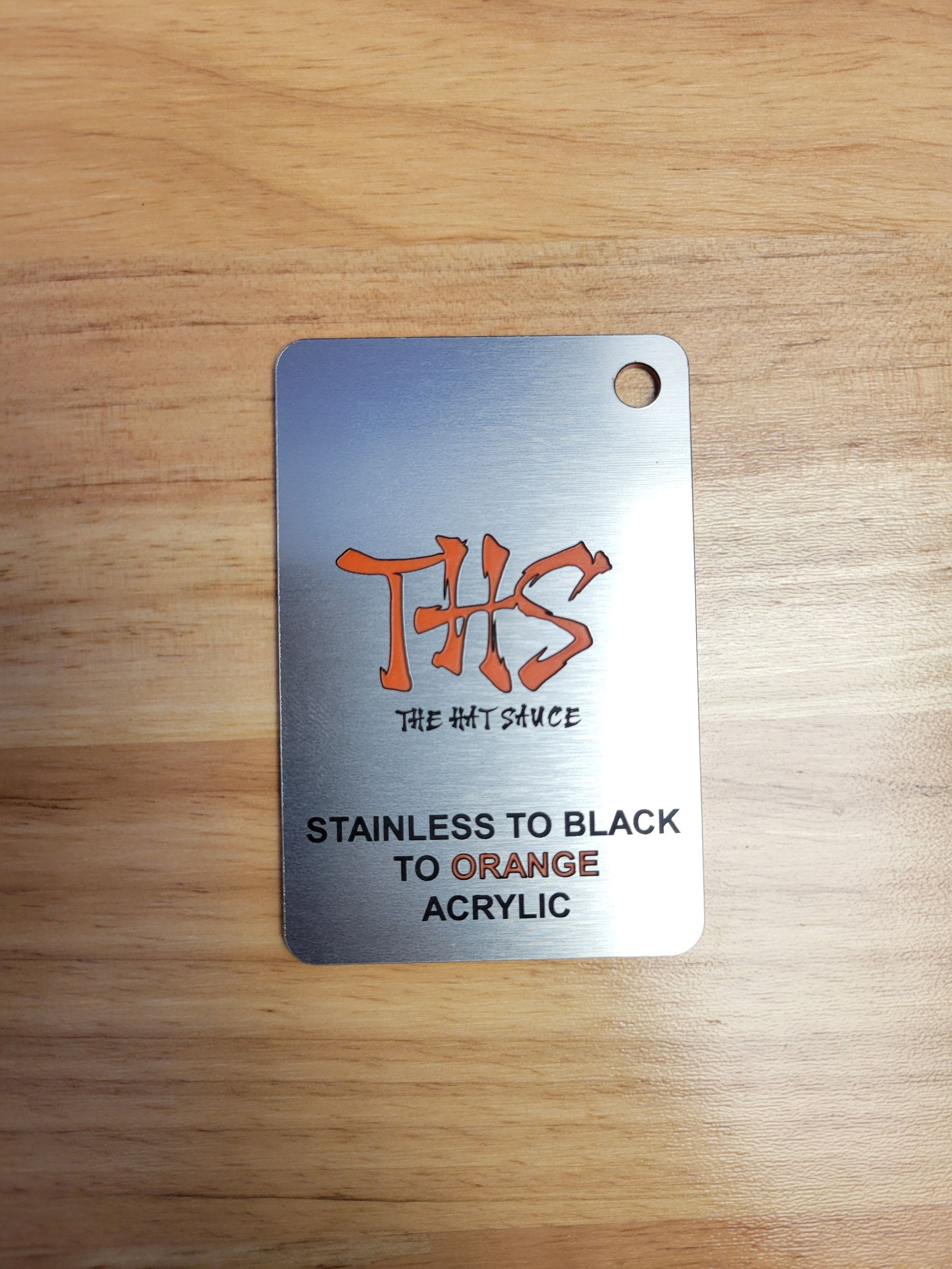 A stainless to black to orange acrylic tag is sitting on a wooden table.
