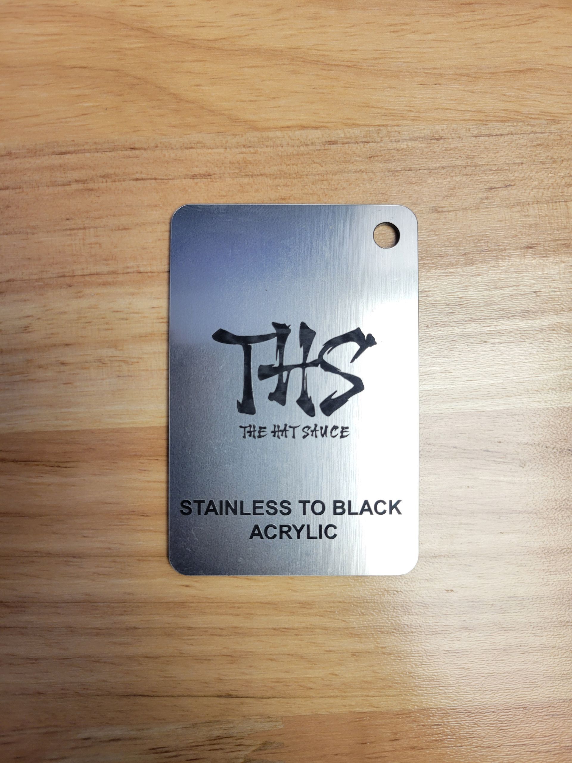A stainless to black acrylic tag is sitting on a wooden table.