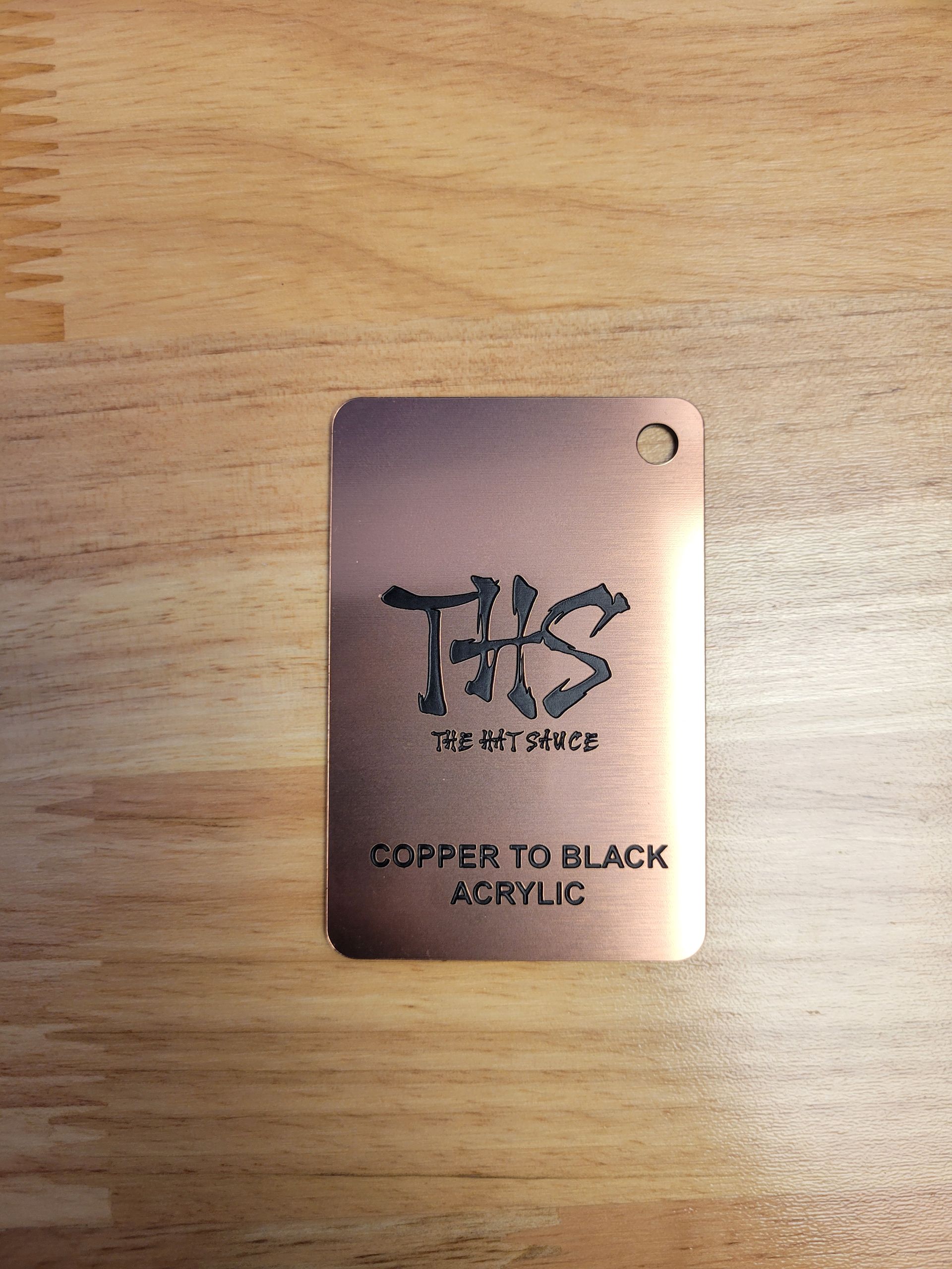 A copper to black acrylic tag is sitting on a wooden table.