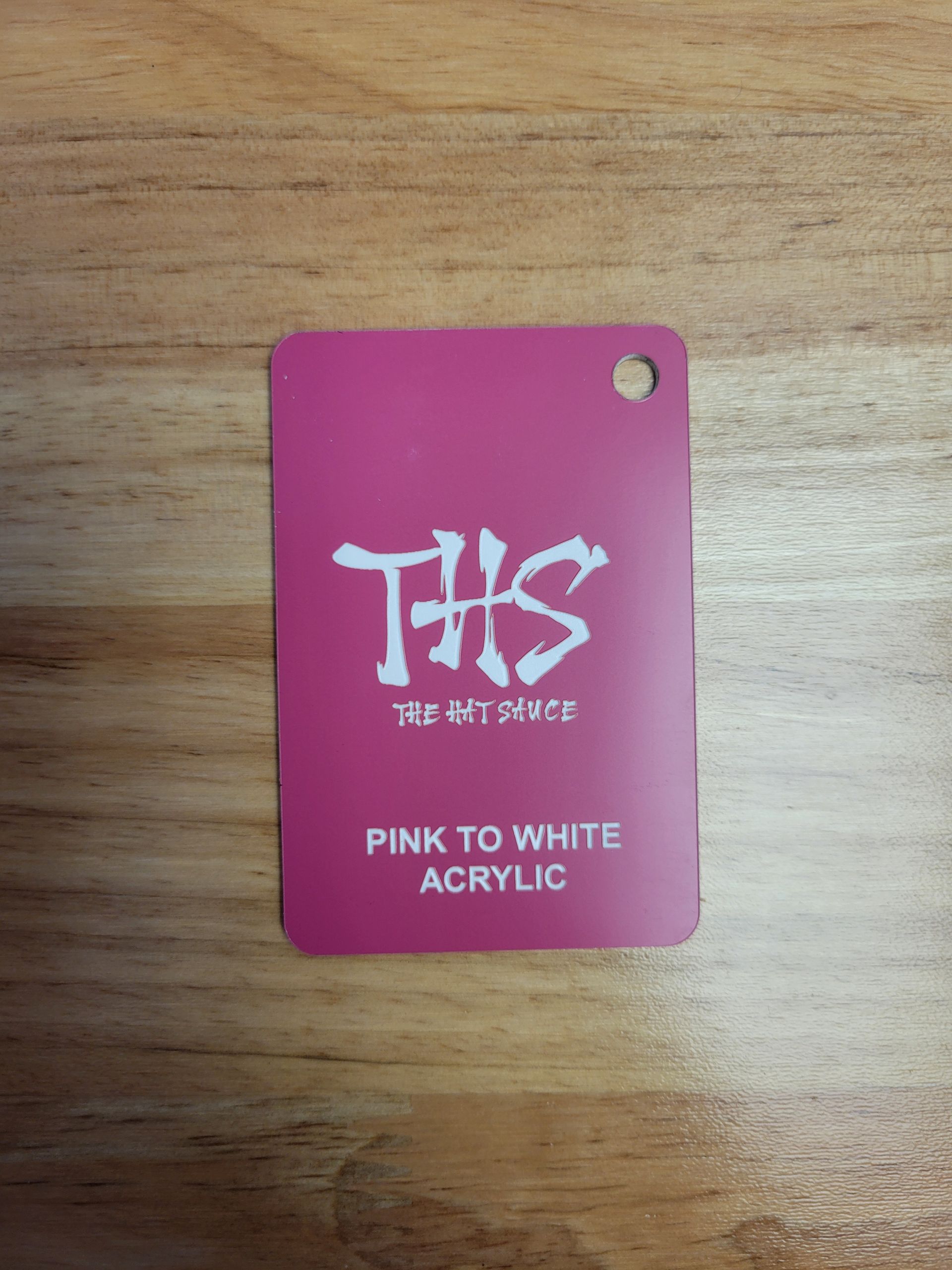 A pink to white acrylic tag is on a wooden table