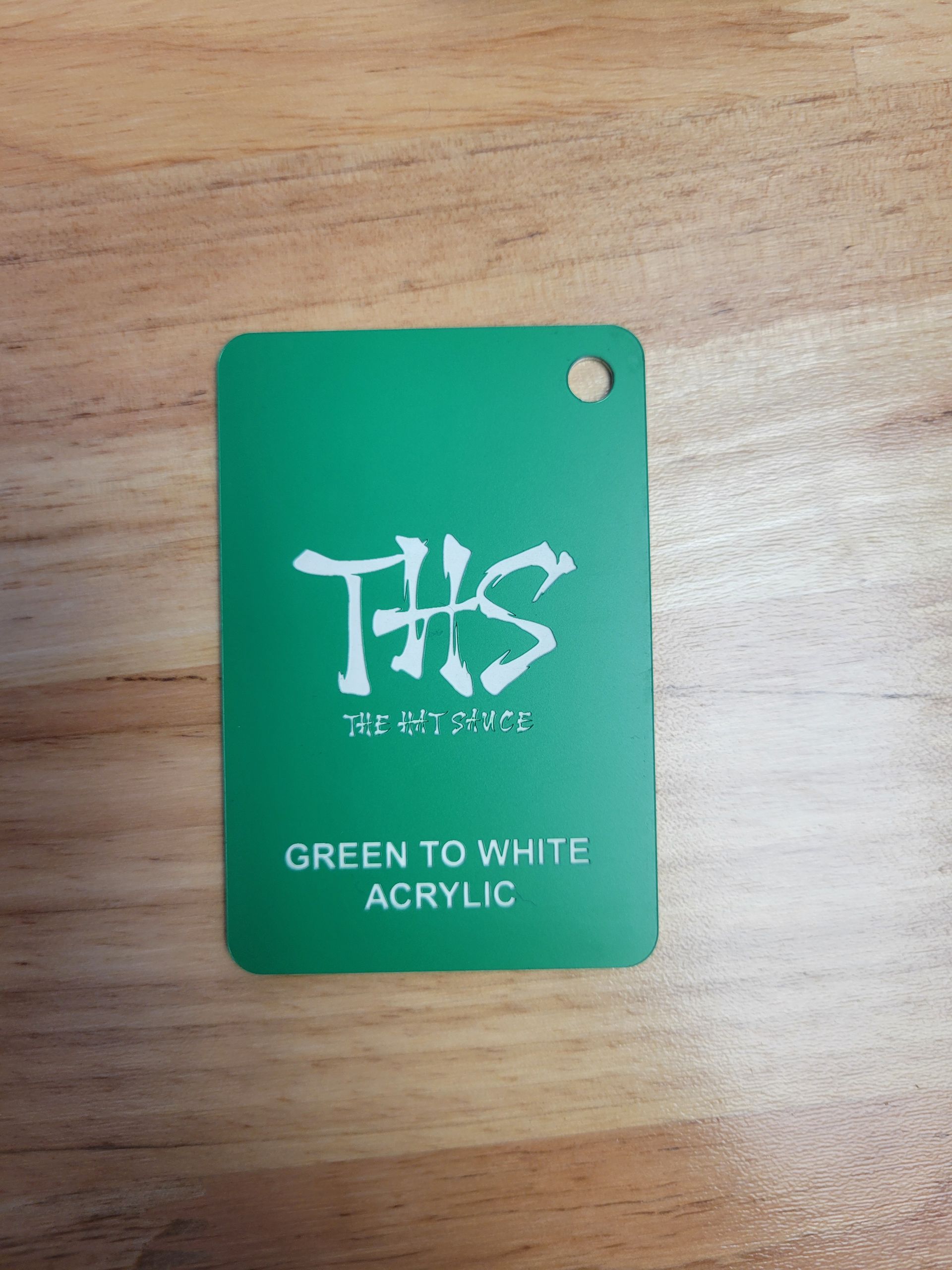 A green to white acrylic tag is on a wooden table