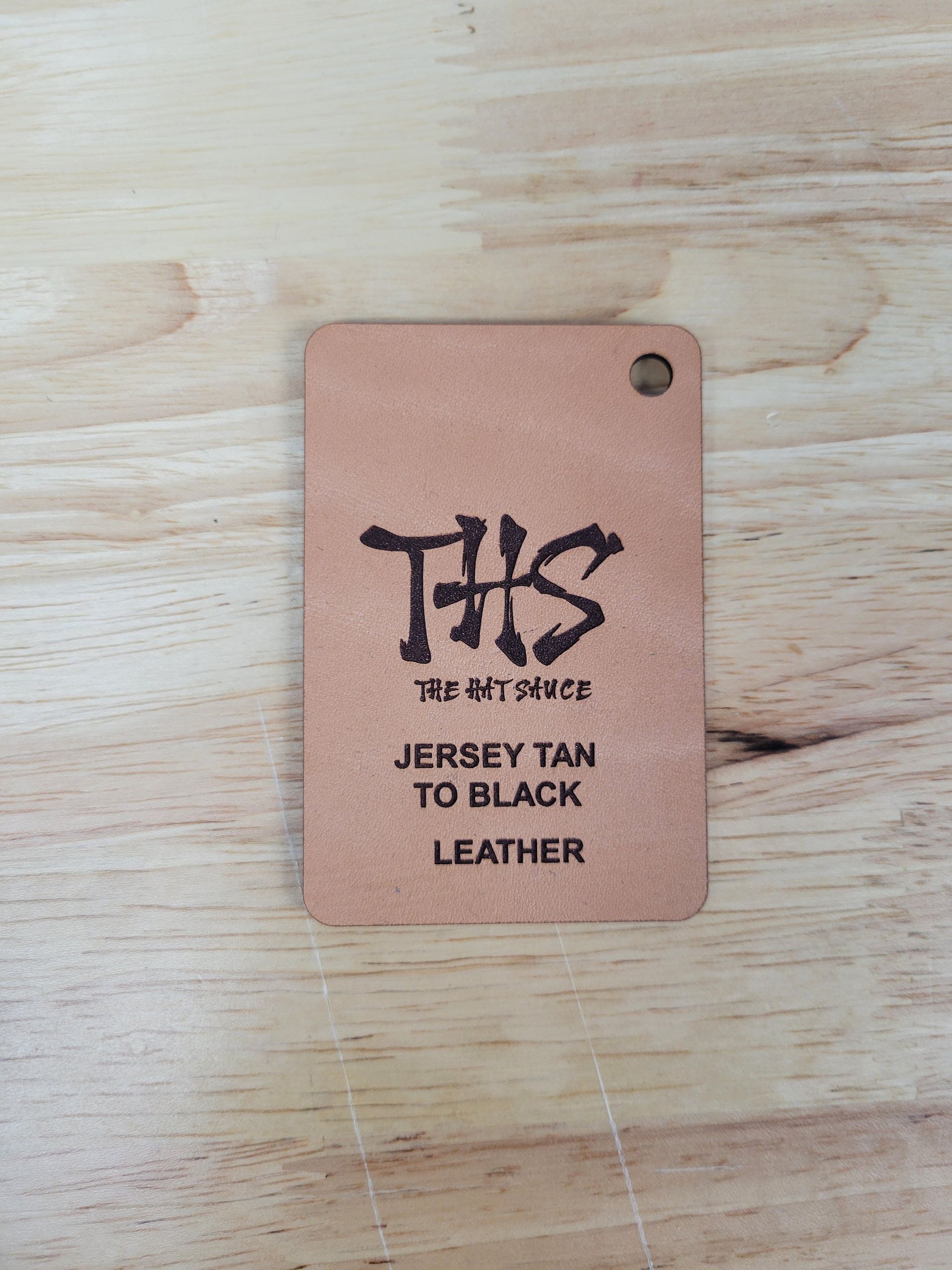 A tag that says this jersey tan to black leather is on a wooden table.