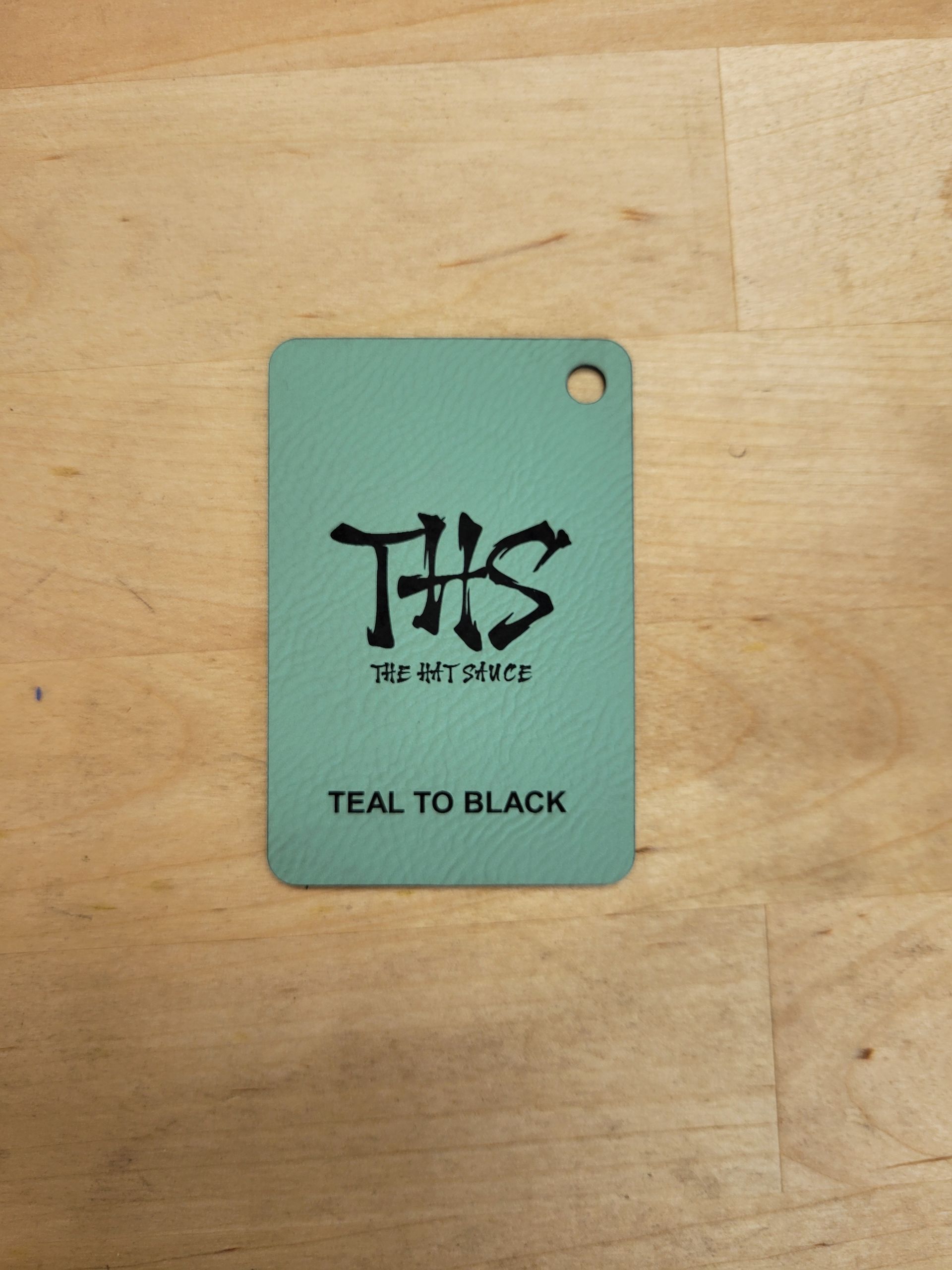 A teal to black tag is on a wooden surface