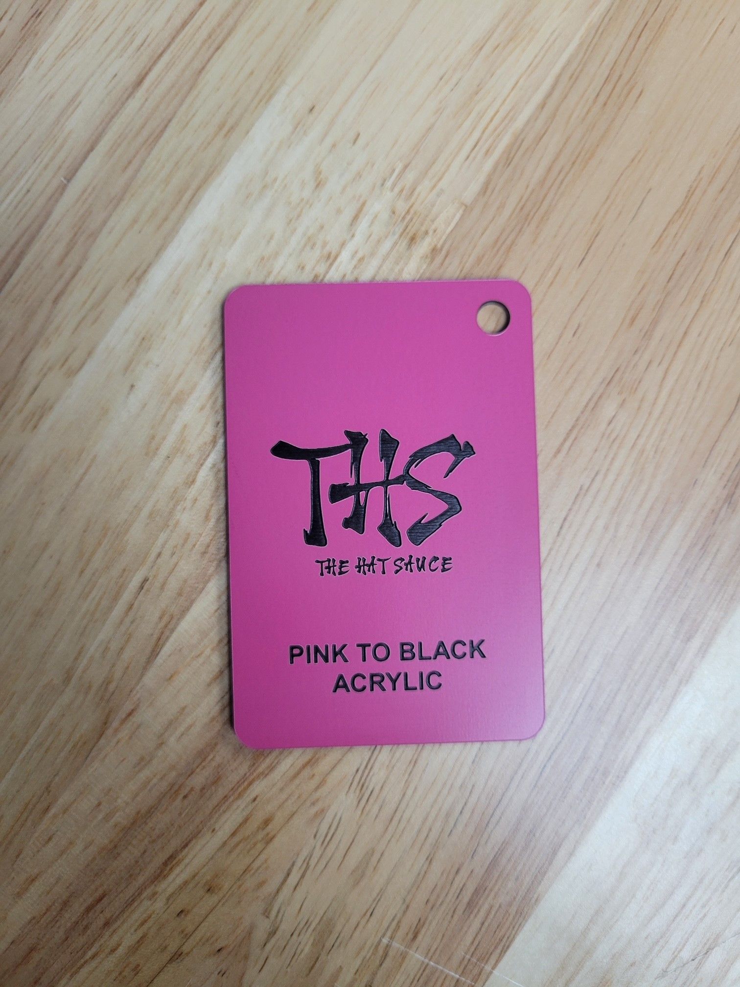 A pink to black acrylic tag is sitting on a wooden table.