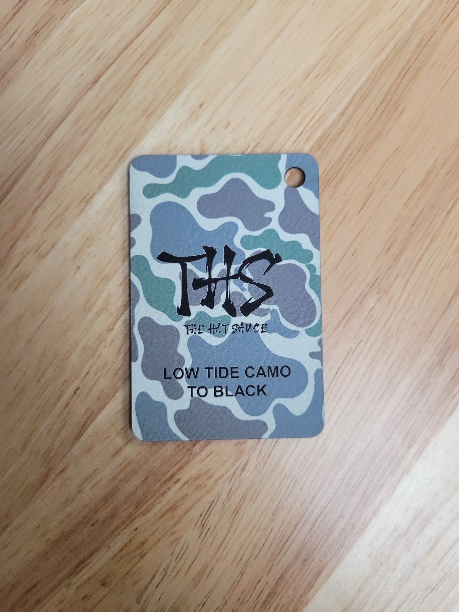 A tag with a camouflage pattern is sitting on a wooden table.