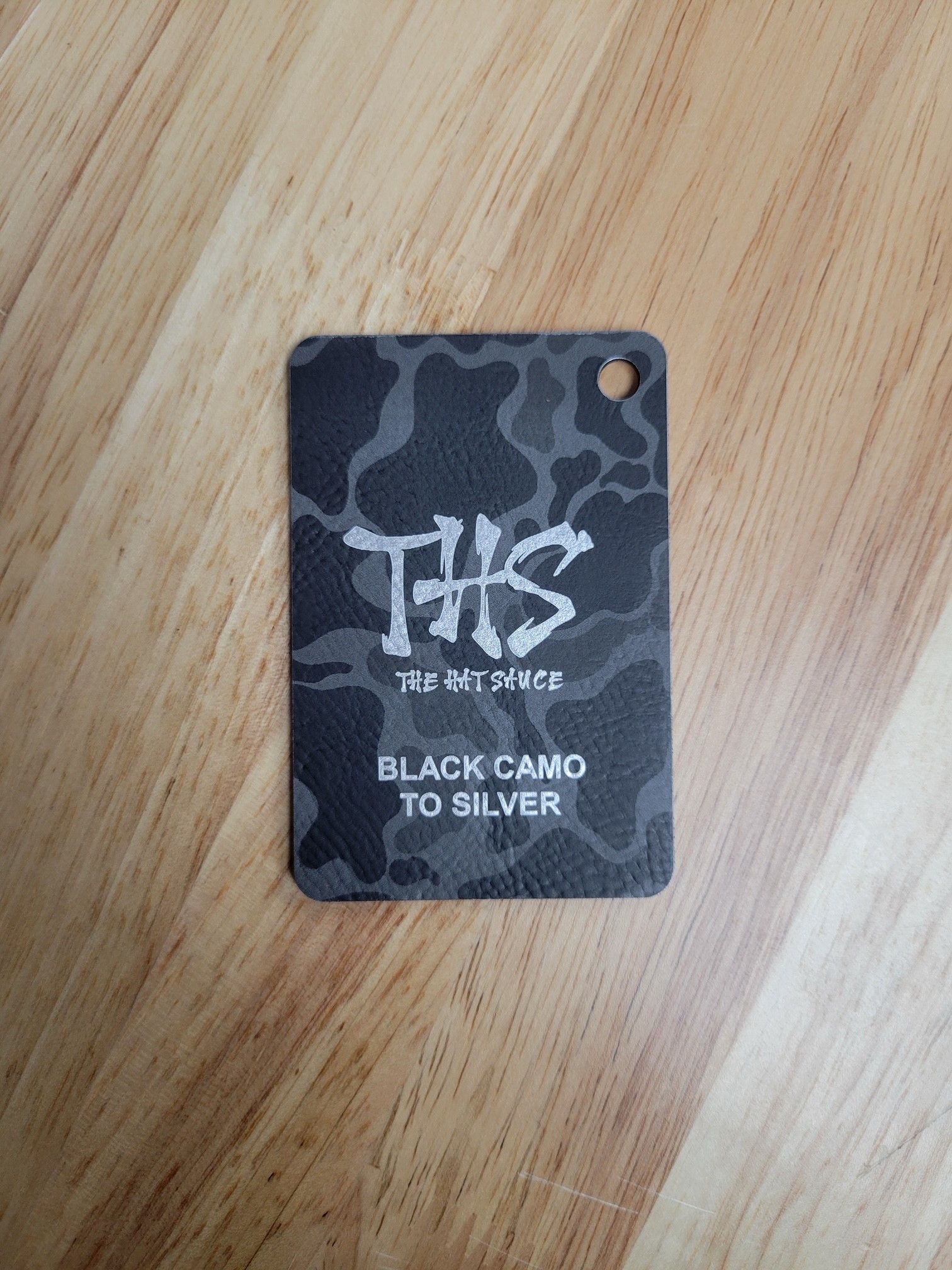 A black camo to silver tag is sitting on a wooden table.