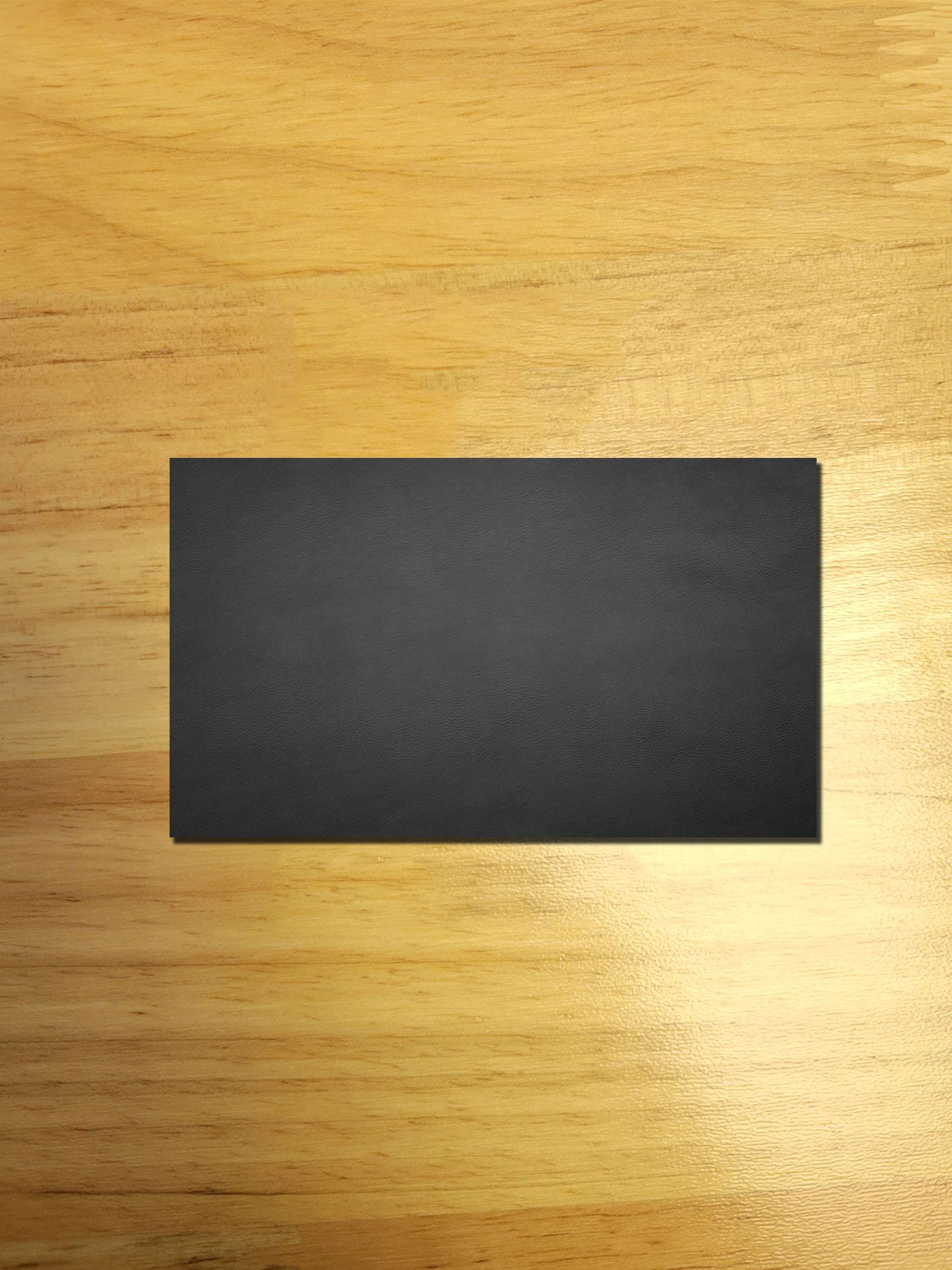 A black business card is sitting on a wooden table.