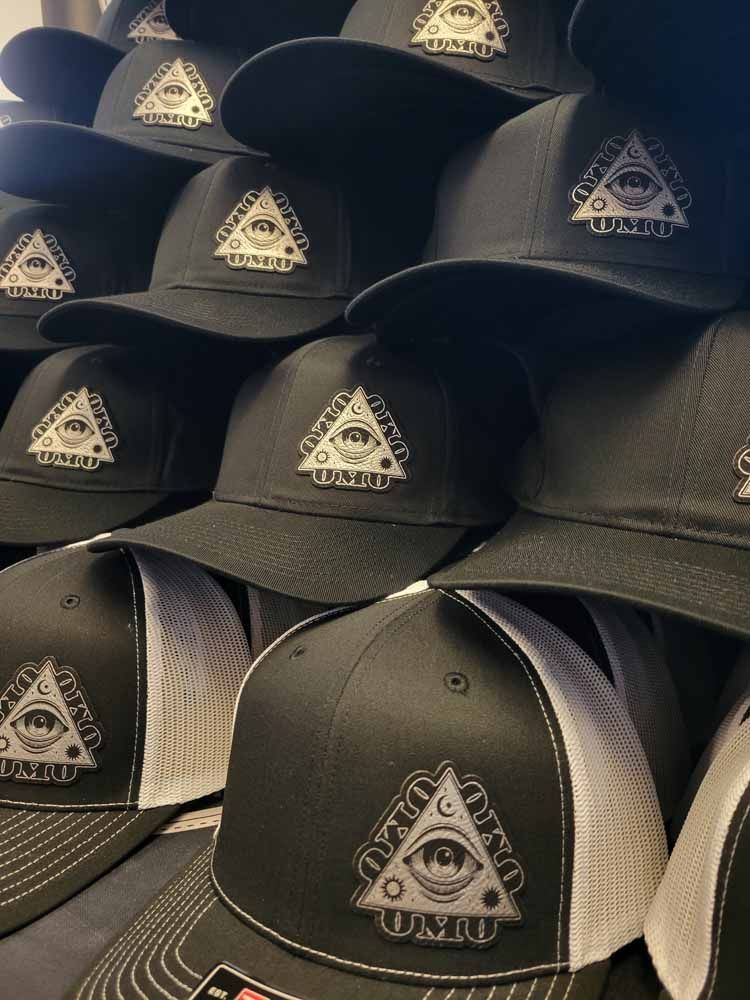 A stack of black hats with an all seeing eye on them