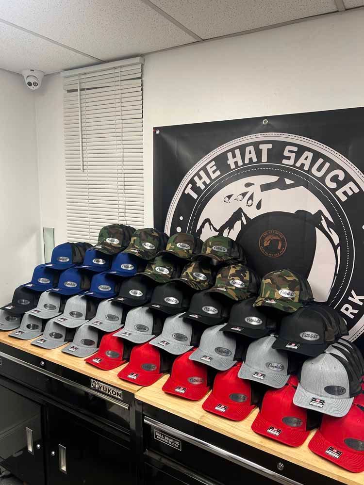 A bunch of hats are sitting on a table in front of a sign that says the hat sauce.