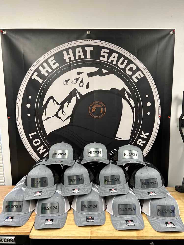 A bunch of hats are sitting on a table in front of a sign that says `` the hat sauce ''.