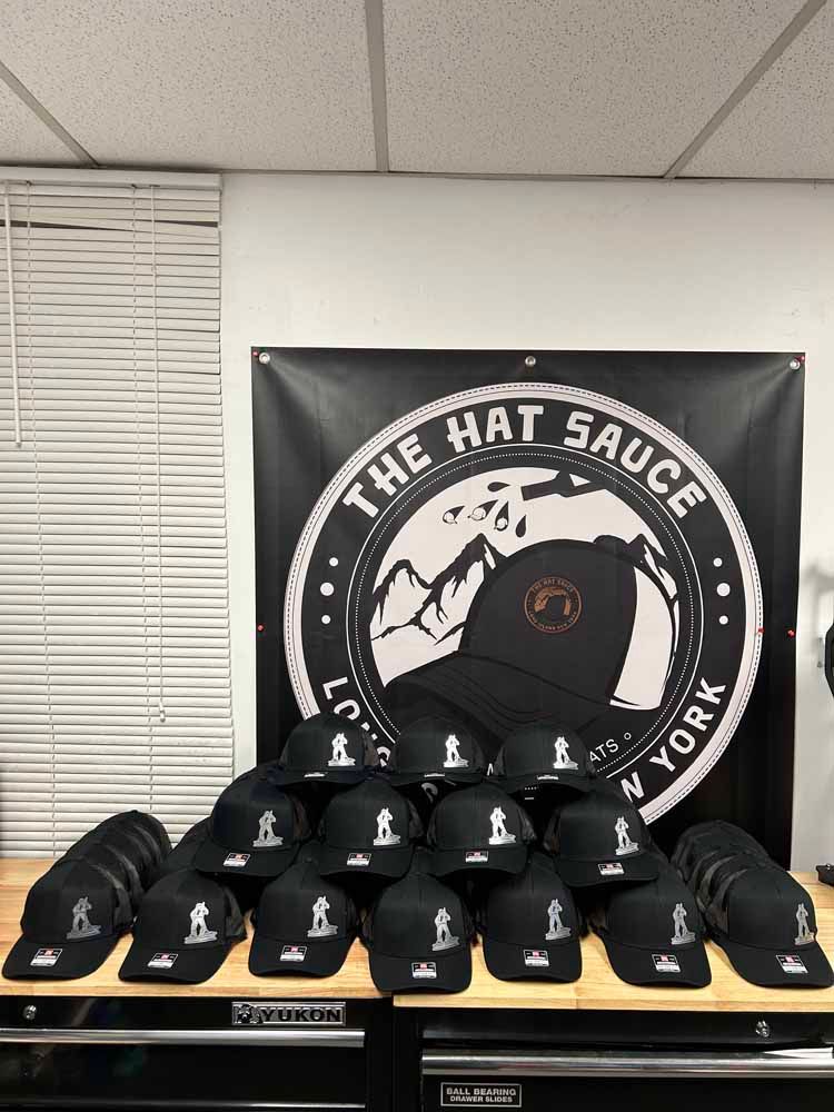 A bunch of hats are sitting on a table in front of a sign that says the hat sauce ny york