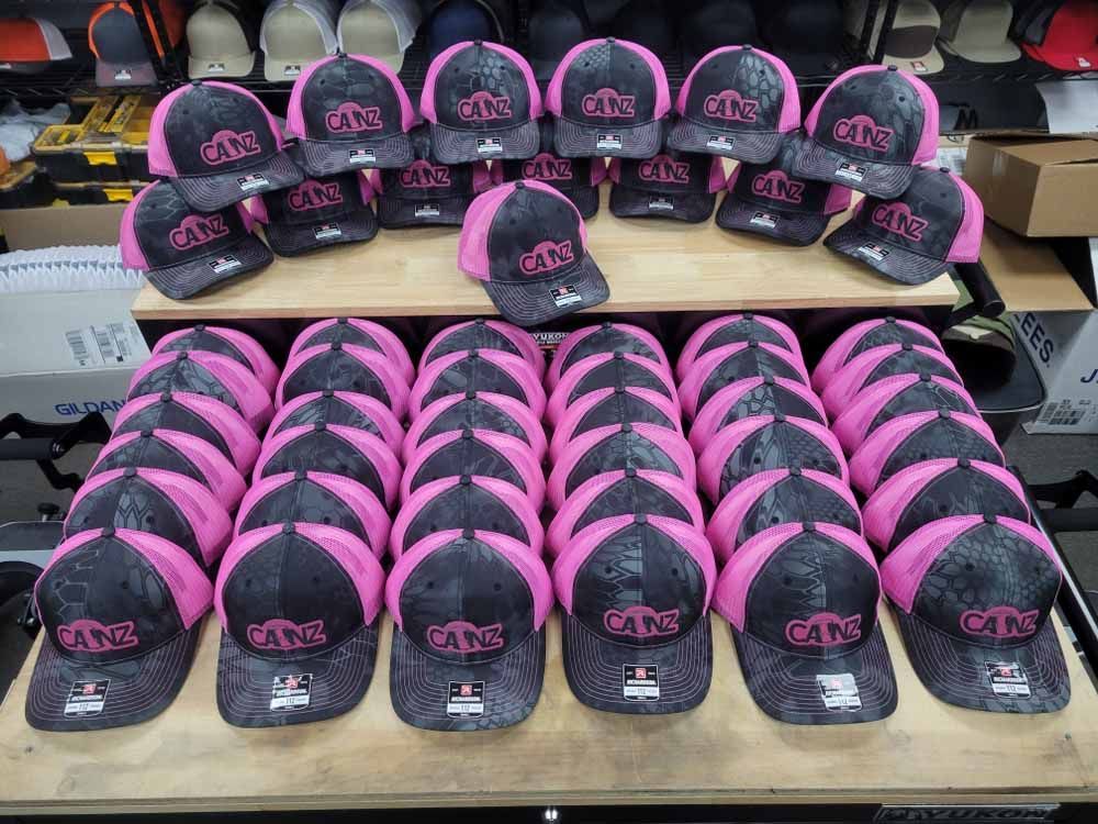 A bunch of pink and black hats are sitting on a wooden table.