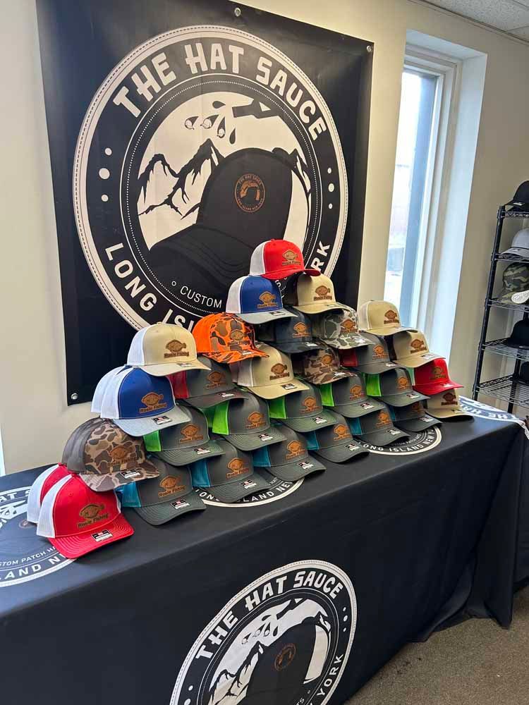 A bunch of hats are sitting on a table in front of a sign that says the hat sauce long island.