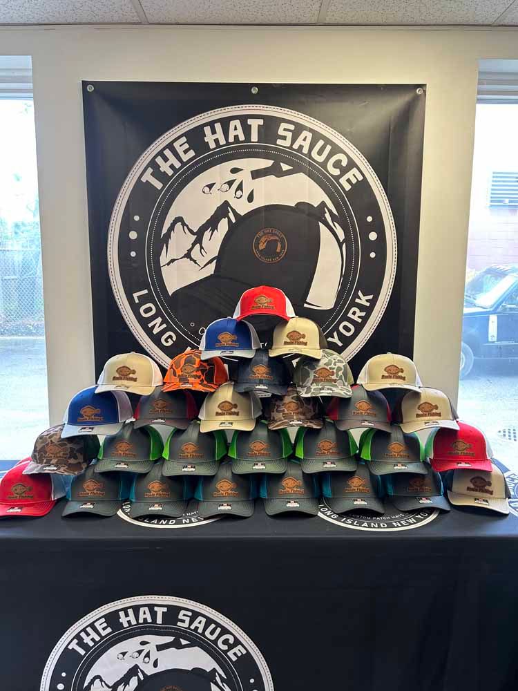 A bunch of hats are on a table in front of a sign that says the hat sauce