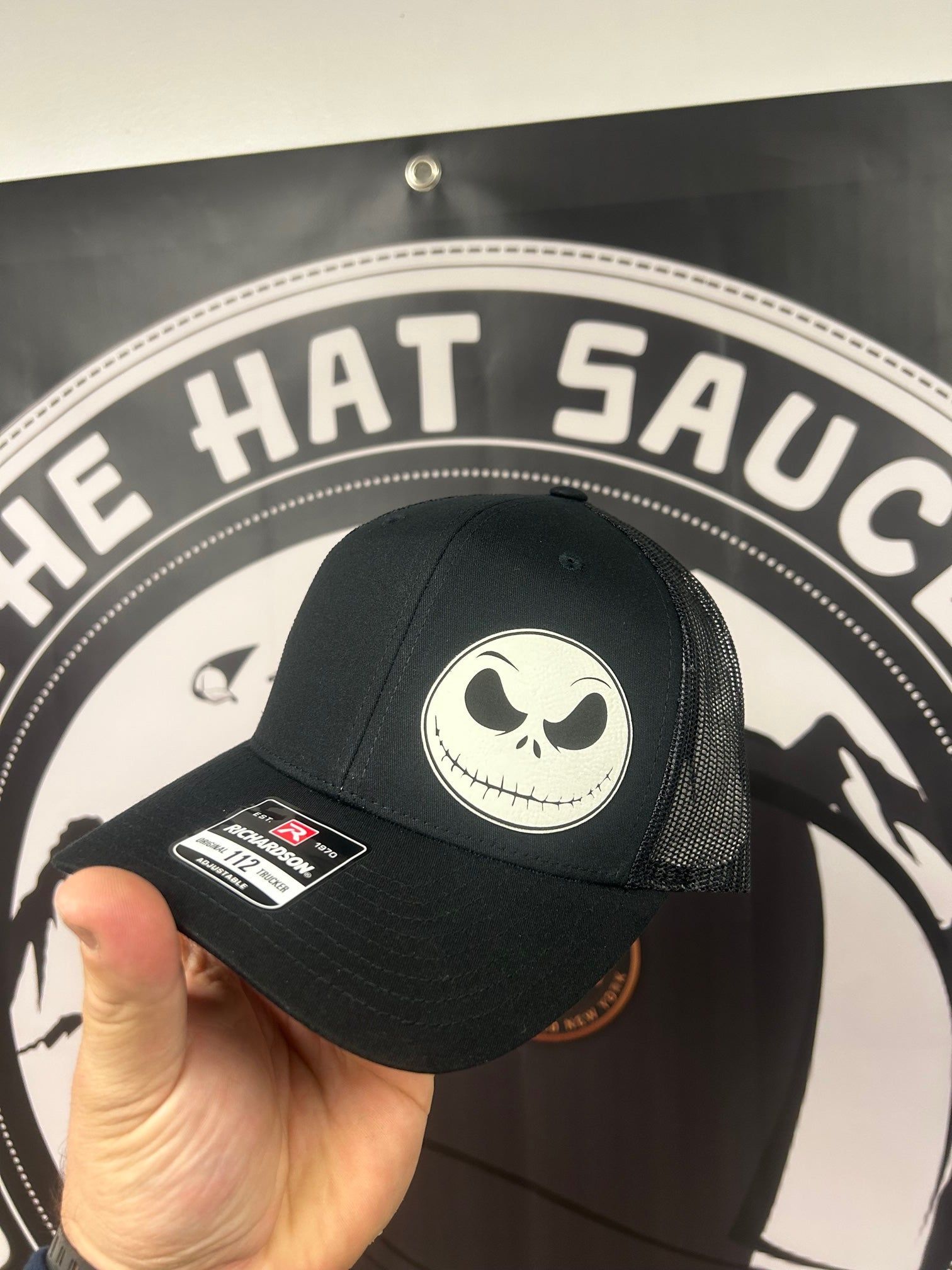 A person is holding a hat in front of a sign that says the hat sauce