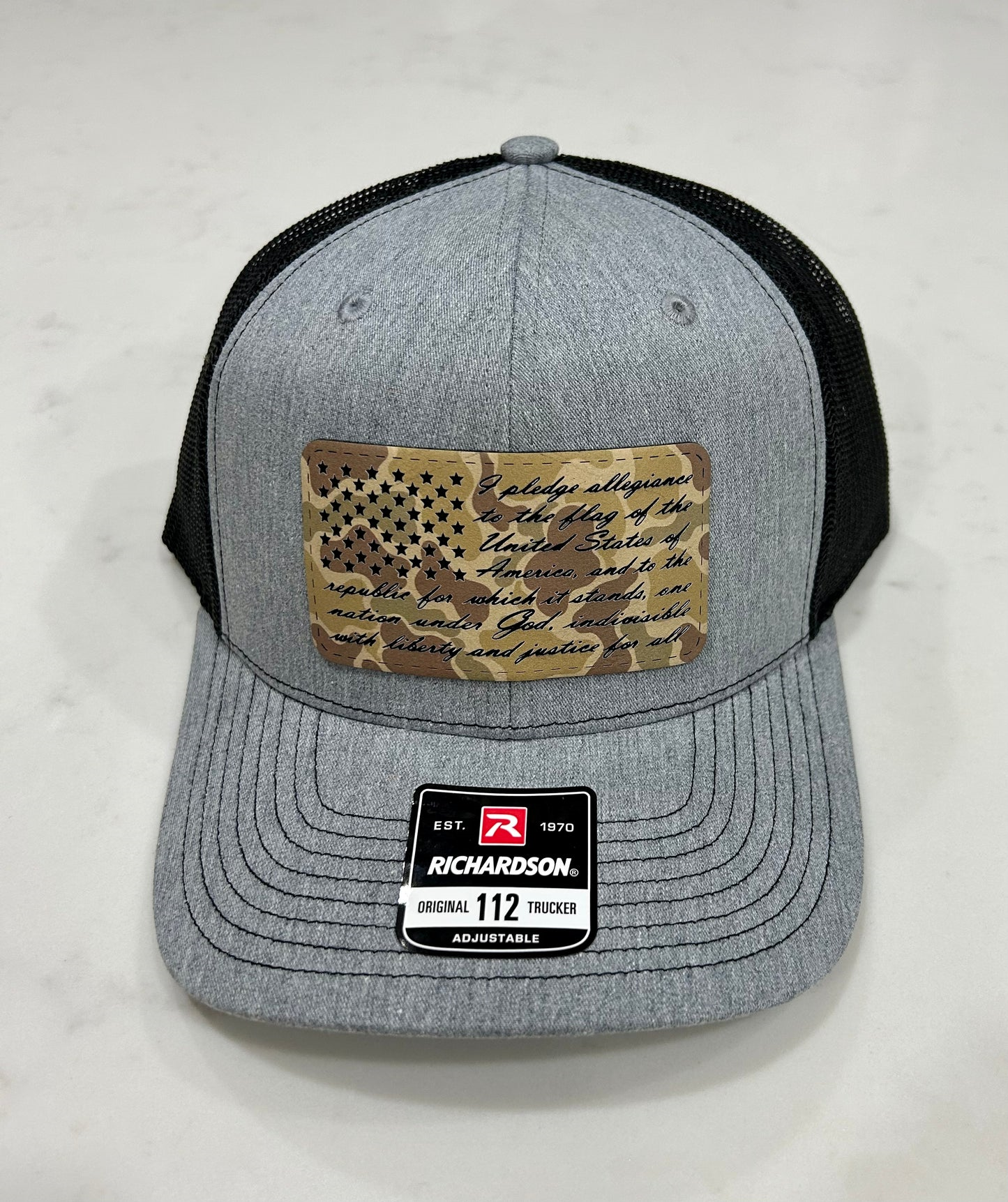 A gray and black baseball cap with a camouflage american flag on it.