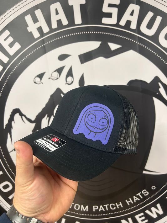 A person is holding a black hat with a purple ghost on it