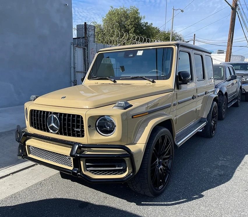 Beige Mercedes-Benz G-Wagon parked on a street beside a blue building.