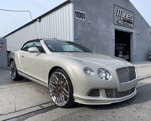 White Bentley convertible parked outside a garage with dark walls and signage