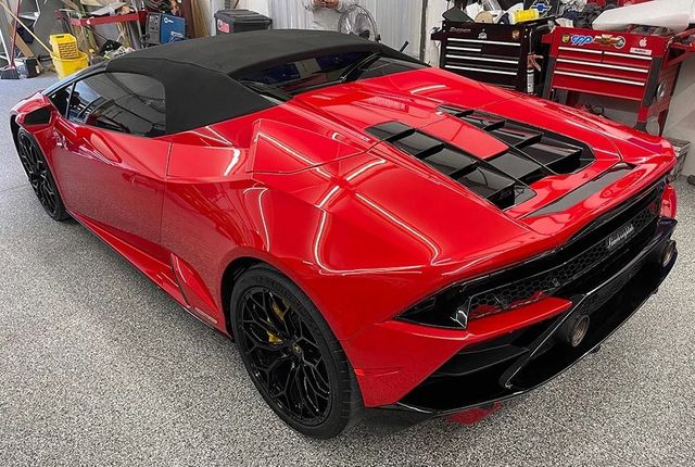 Red sports car in a garage, shown from the rear with a black roof and engine cover vents.