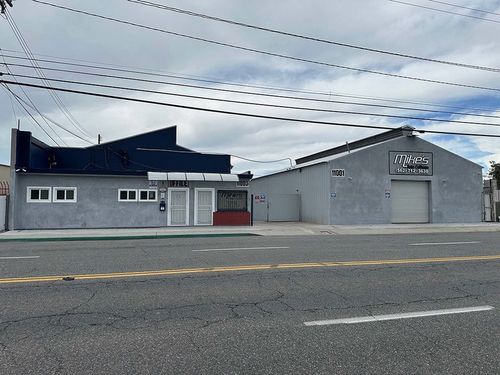 Gray industrial buildings along a roadside under a cloudy sky, with power lines overhead.