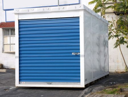 Blue-doored storage unit in a parking lot. White walls, metal roll-up door, lock.