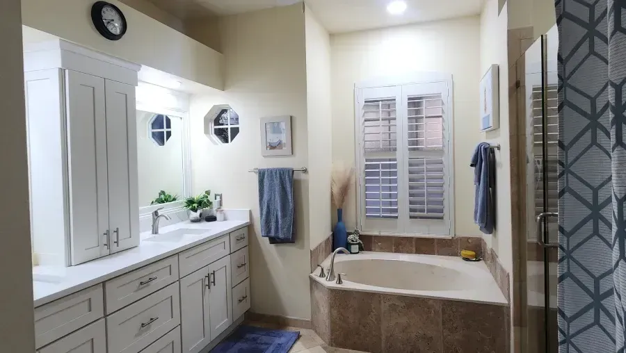 Bathroom with white cabinets, tub, and window with shutters.