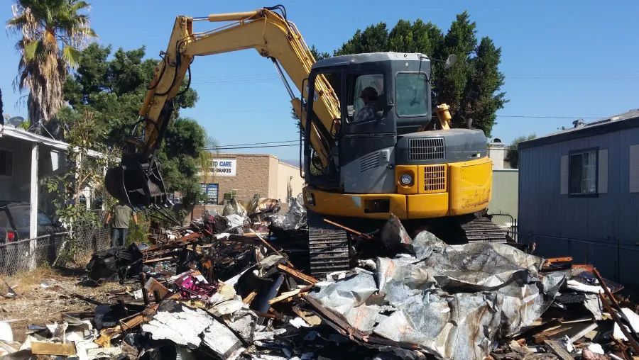 Yellow excavator demolishing a building on a sunny day.