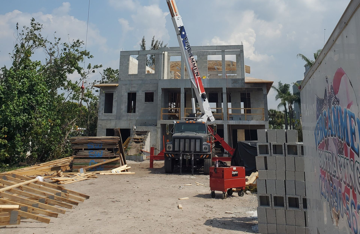 A construction site features a crane working on a multi-story concrete building under a sunny sky.