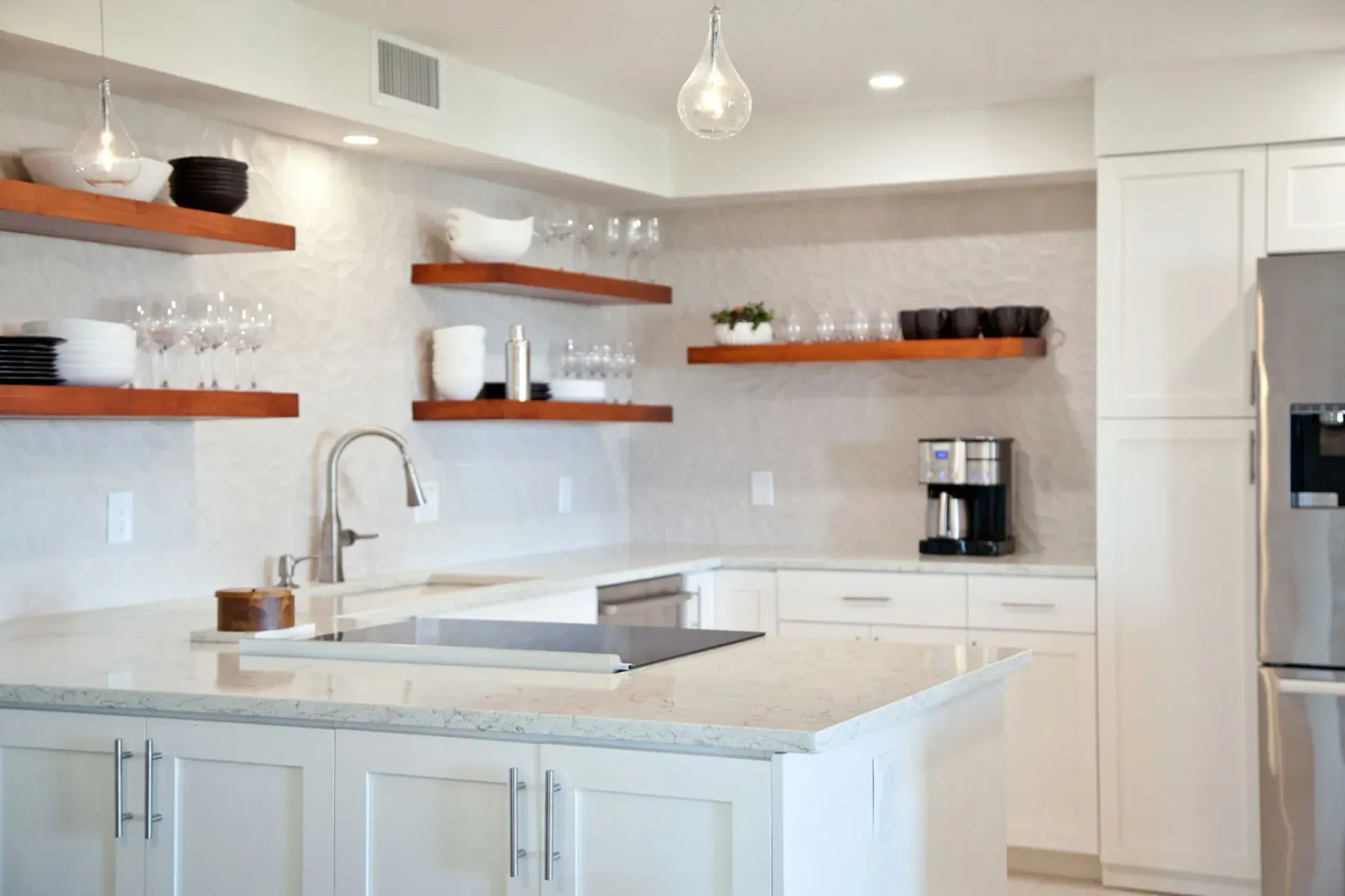 Modern white kitchen with island, wooden shelves, and stainless steel appliances.