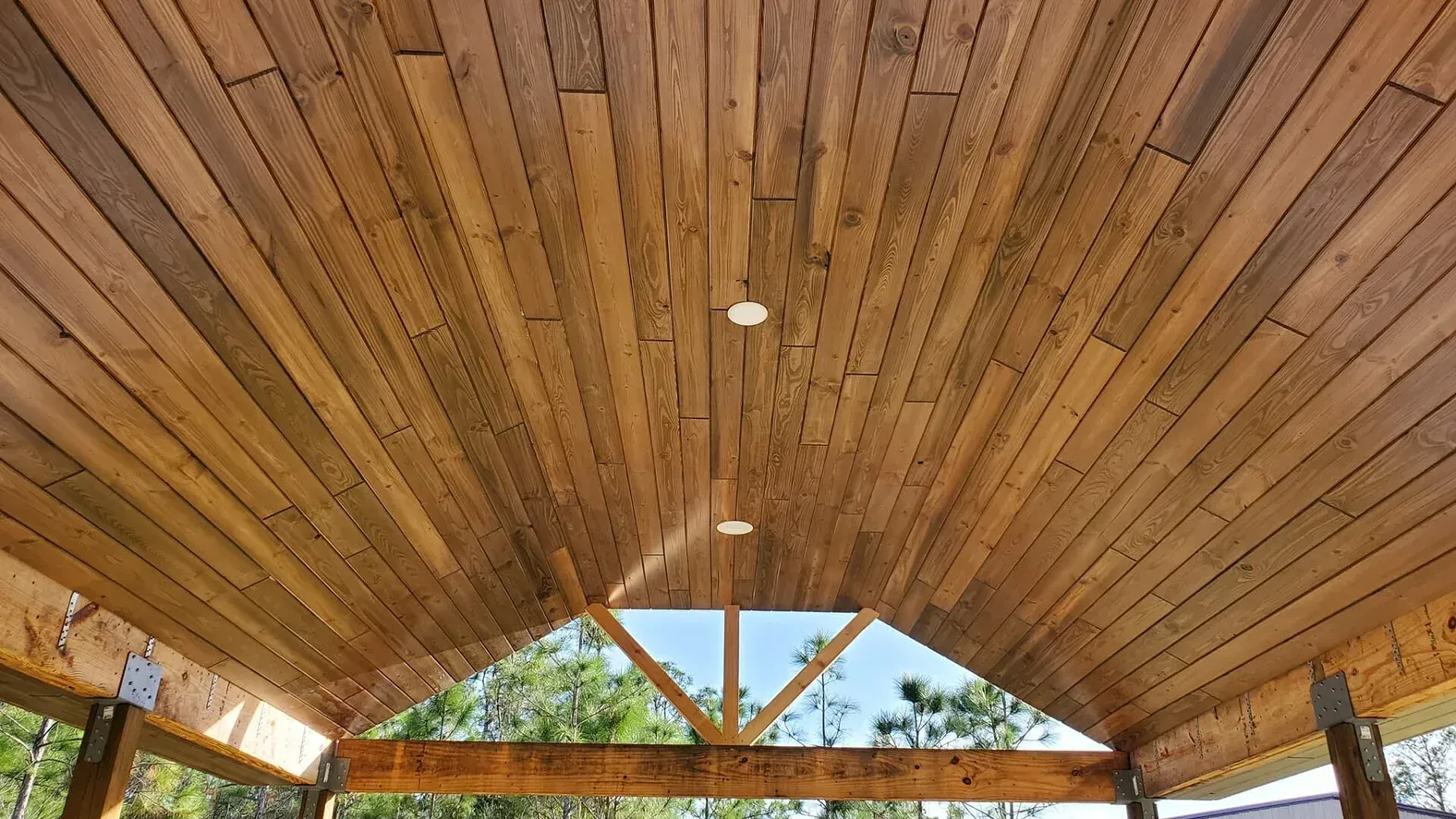 Wooden ceiling of an outdoor covered structure with recessed lights and visible rafters.