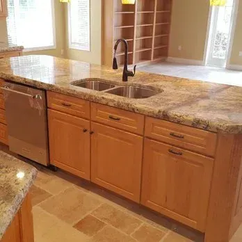 Kitchen island with granite countertop, sink, dishwasher, and wood cabinets.