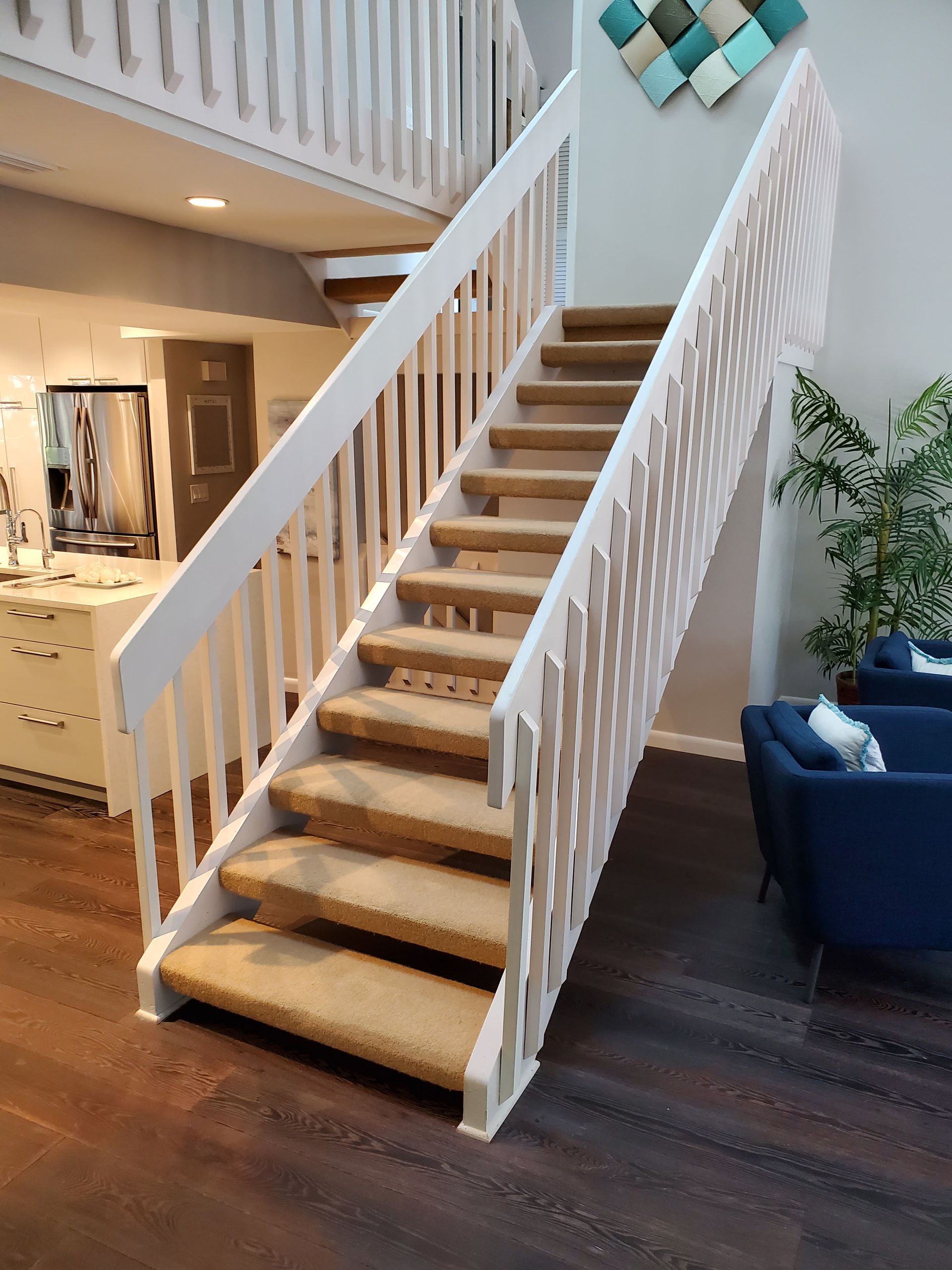 A staircase with tan carpeted steps and white wooden railings in a contemporary, open-plan home.