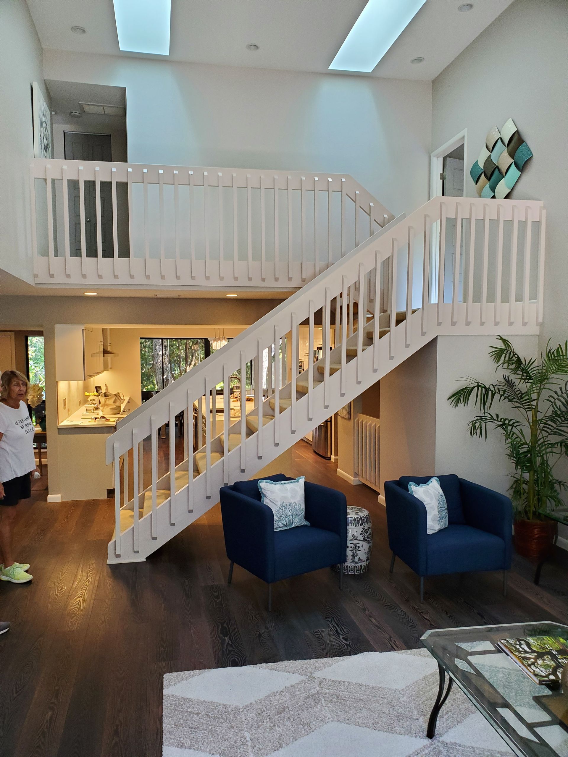 A modern living room with a white staircase, two navy blue armchairs, and dark hardwood floors beneath two skylights.