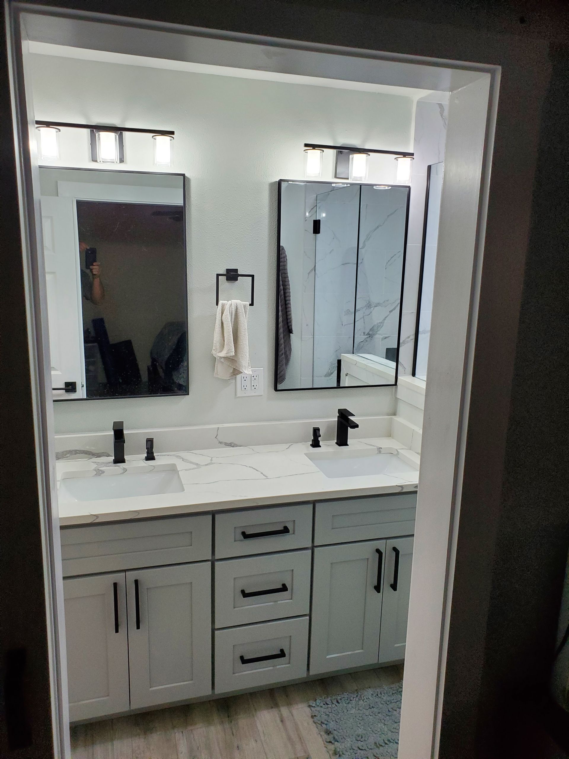 A double-sink bathroom vanity with light gray cabinets, marble-look countertops, two mirrors, and black hardware.