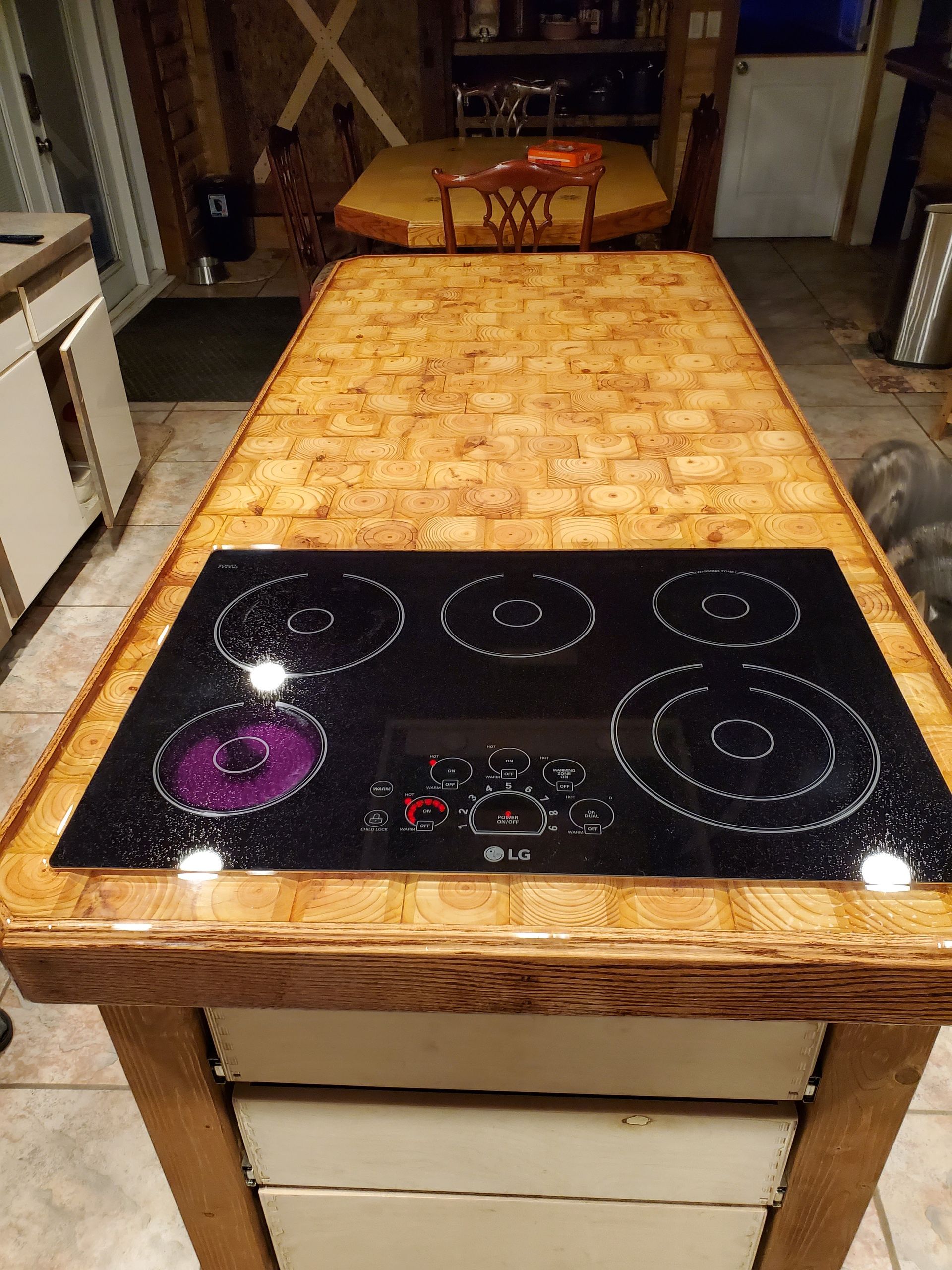A kitchen island with a wood-block surface and a built-in black glass cooktop, viewed from the end of the counter.