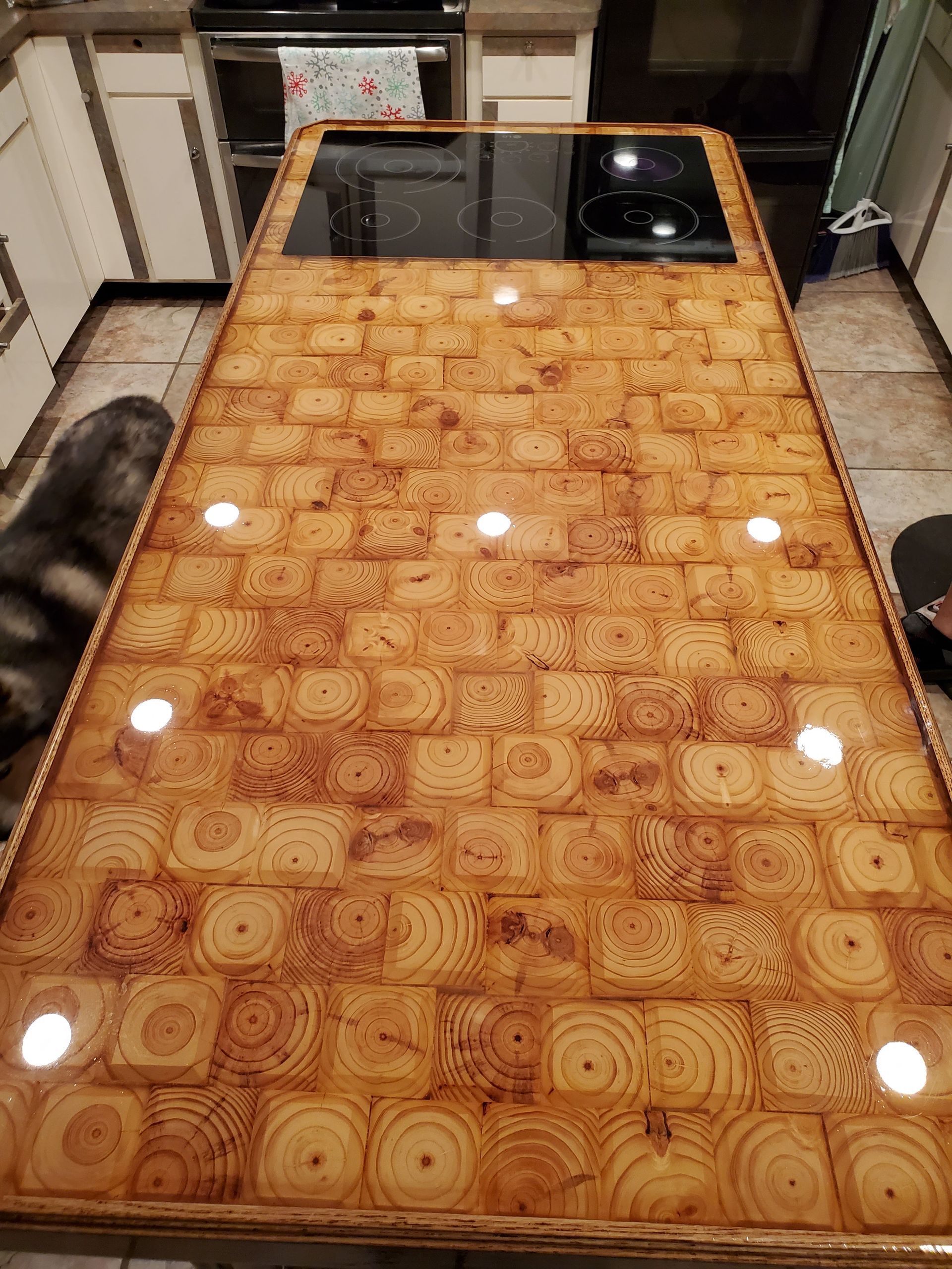 A kitchen island countertop made of polished, resin-coated wood end-grain blocks with an integrated stovetop.