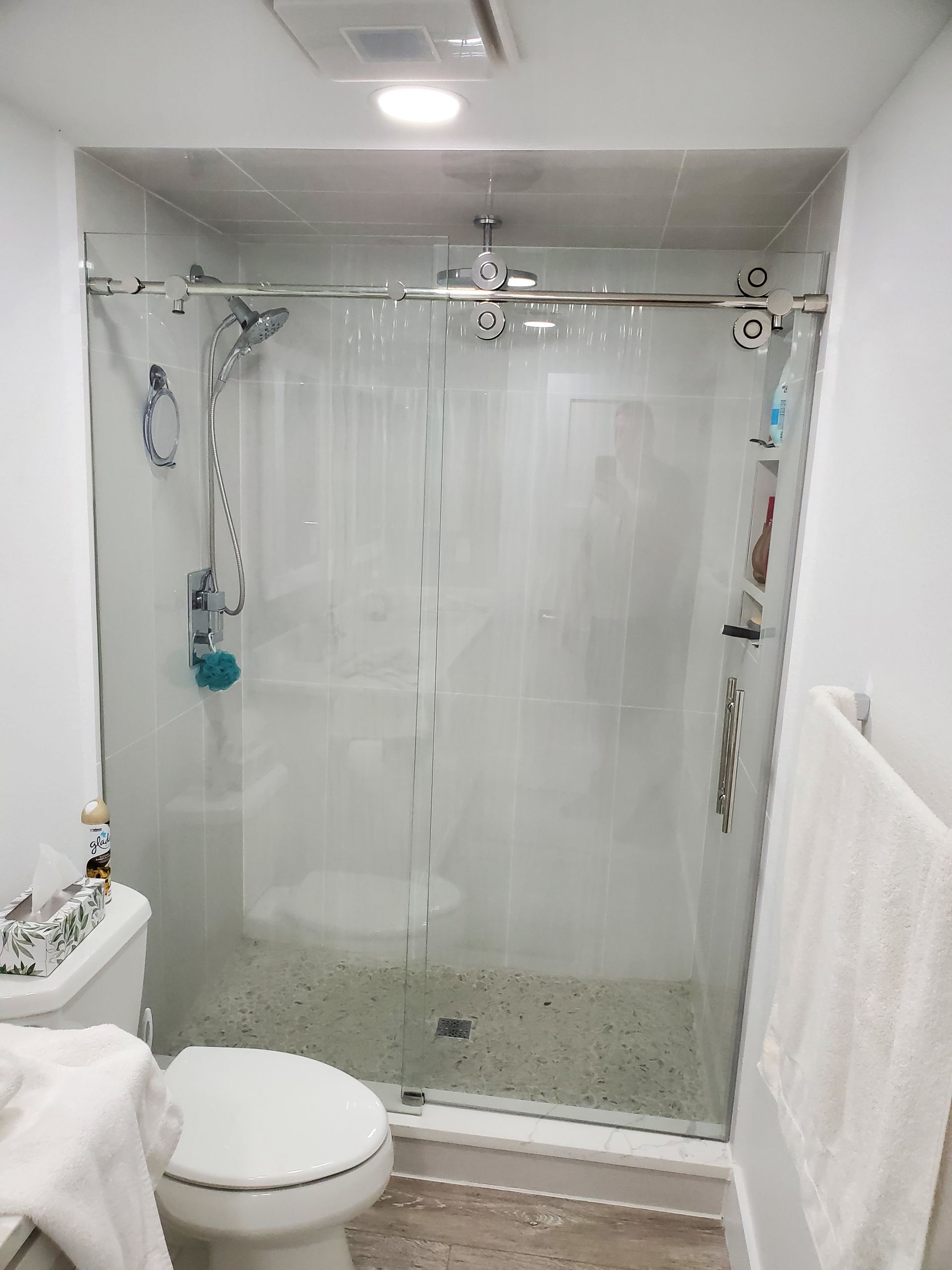 A walk-in shower with clear sliding glass doors, a stone pebble floor, and a polished silver rainfall showerhead.