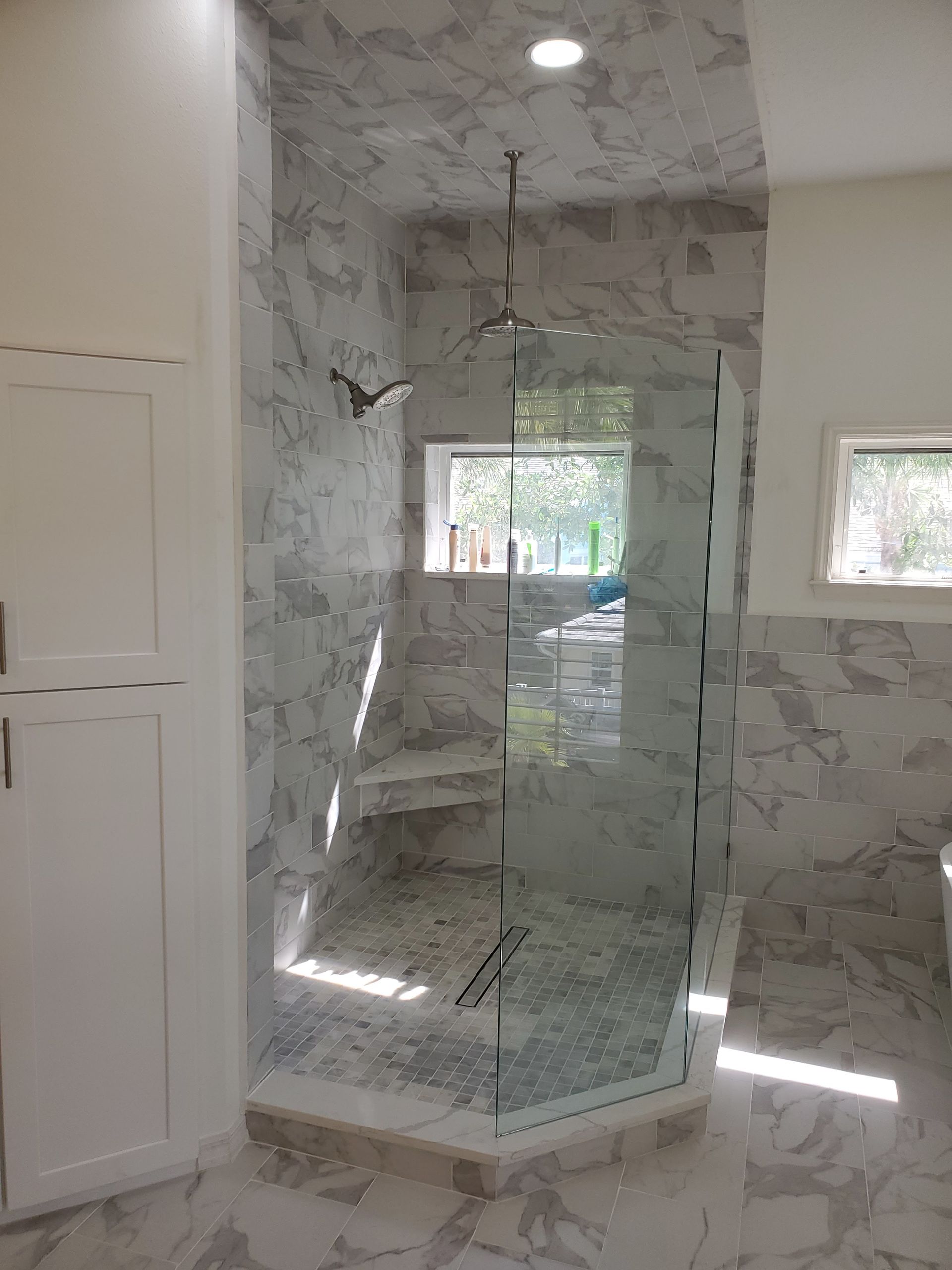 A walk-in shower with light-gray marbled tile, a glass door, a built-in bench, and a rainfall showerhead.