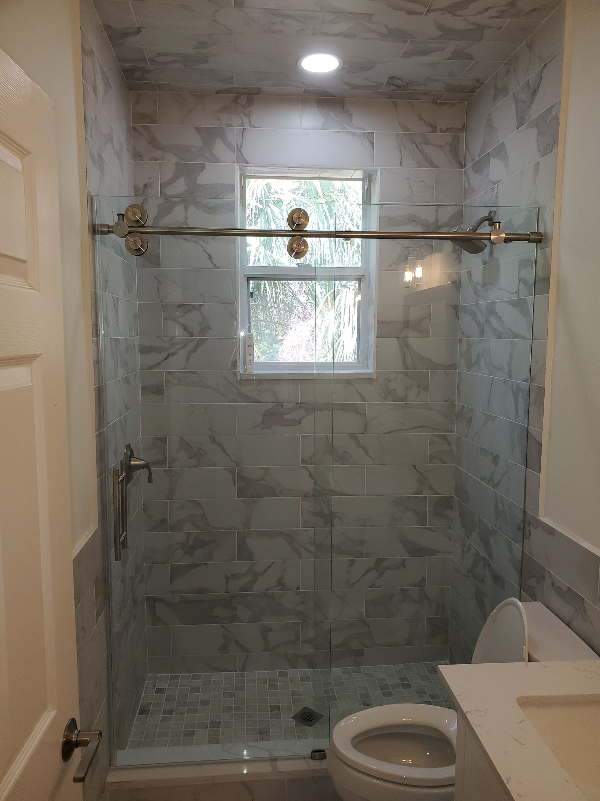 A bathroom featuring a walk-in shower with gray marbled wall tiles, a glass sliding door, and a toilet nearby.