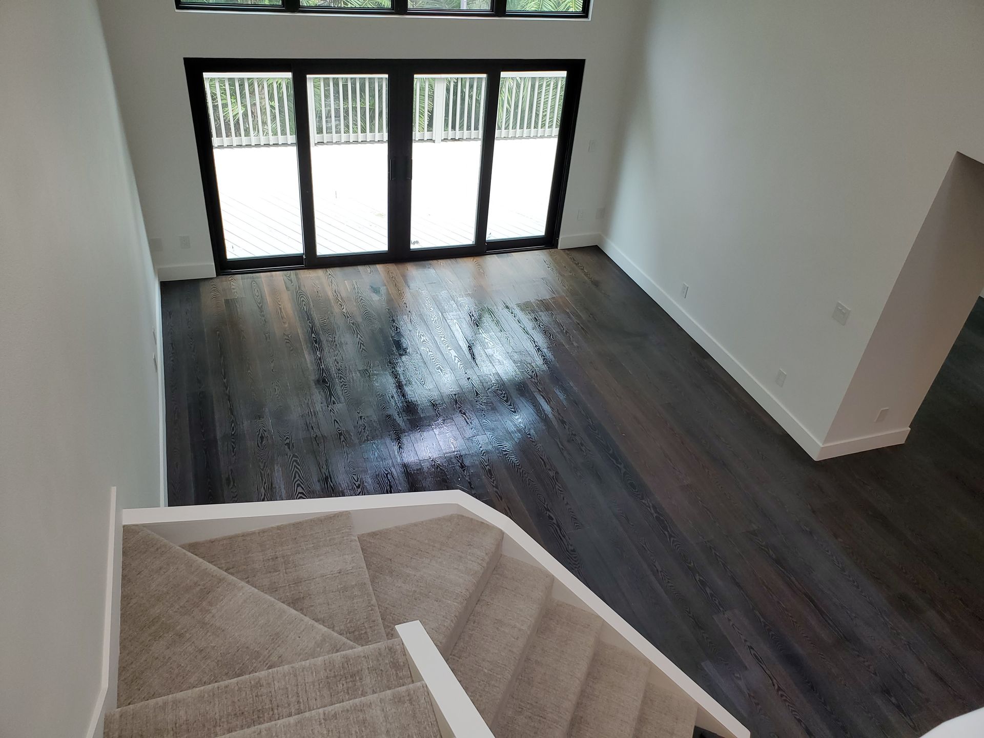 High-angle view of a modern living room with dark hardwood floors, white walls, and a beige carpeted staircase.