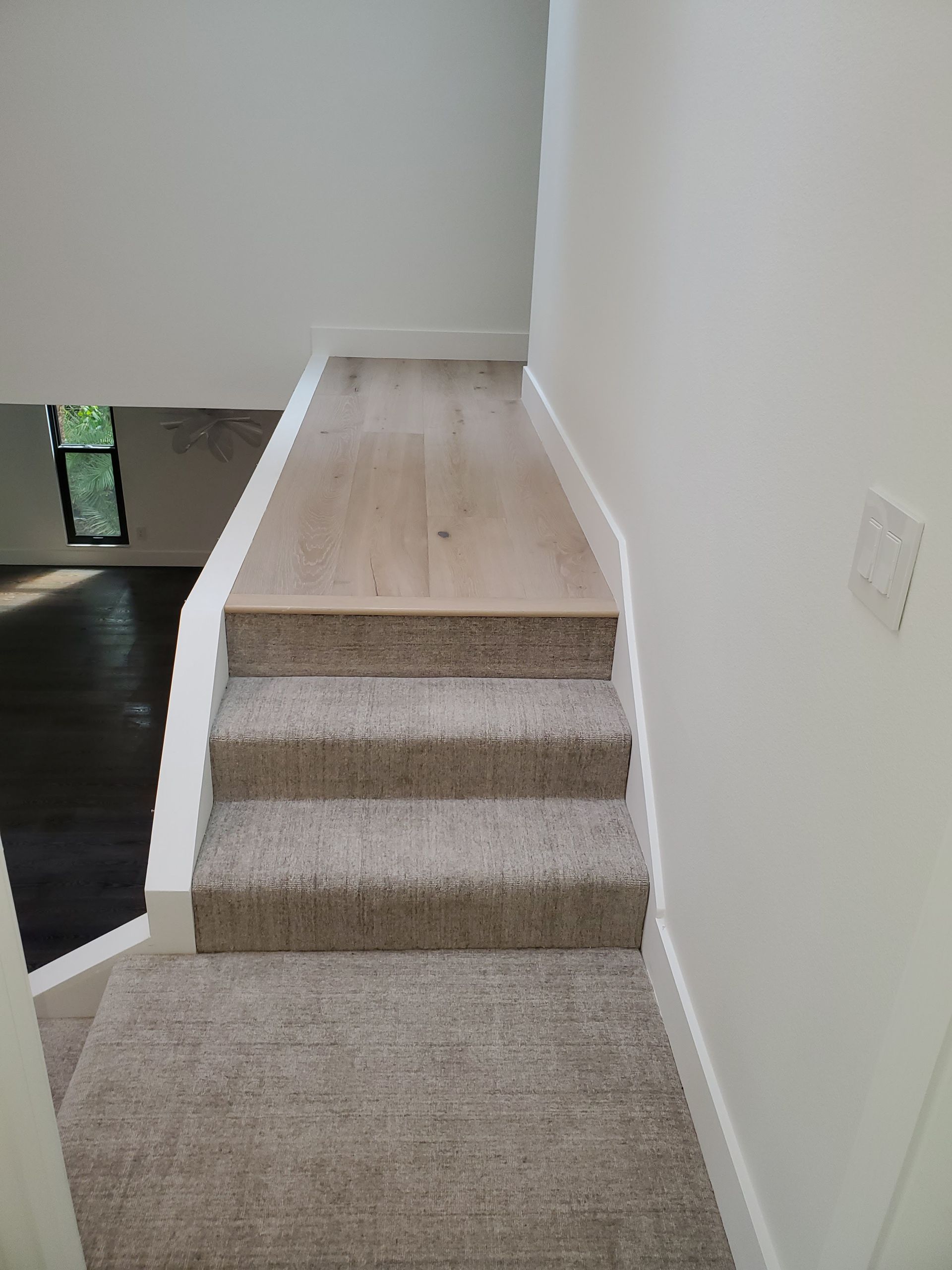 A short staircase with three carpeted steps leading up to a light wood-look floor landing in a white-walled hallway.