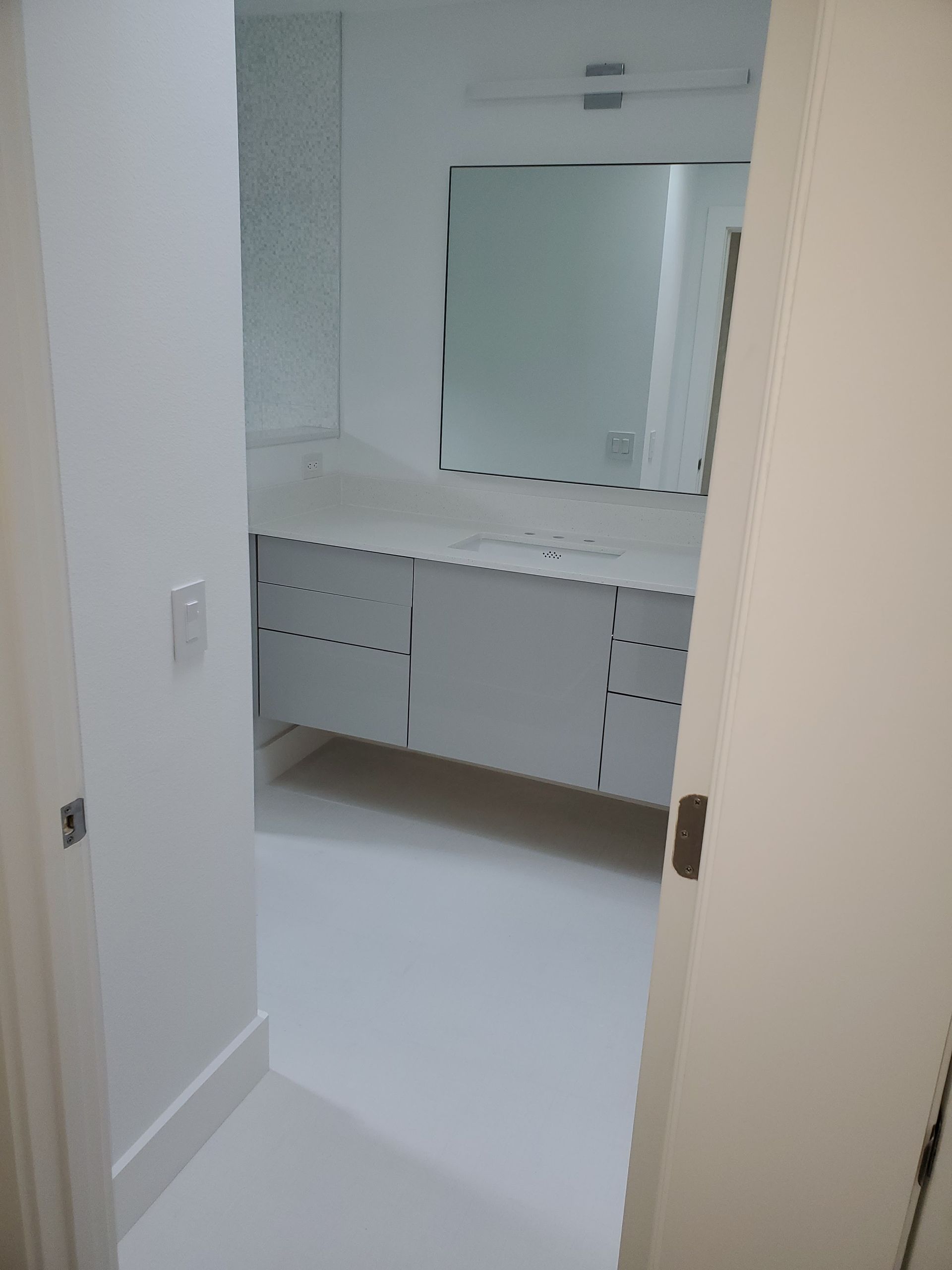 A white bathroom viewed from a doorway, featuring a double vanity cabinet, a wall-mounted mirror, and a light fixture.