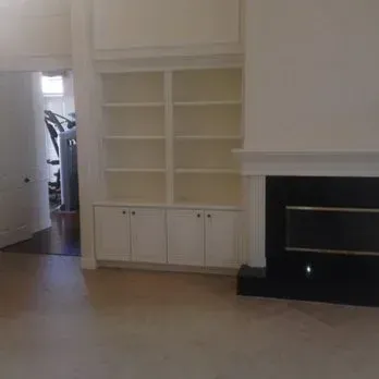 Built-in white bookshelves with cabinets, near a black fireplace and open doorway.