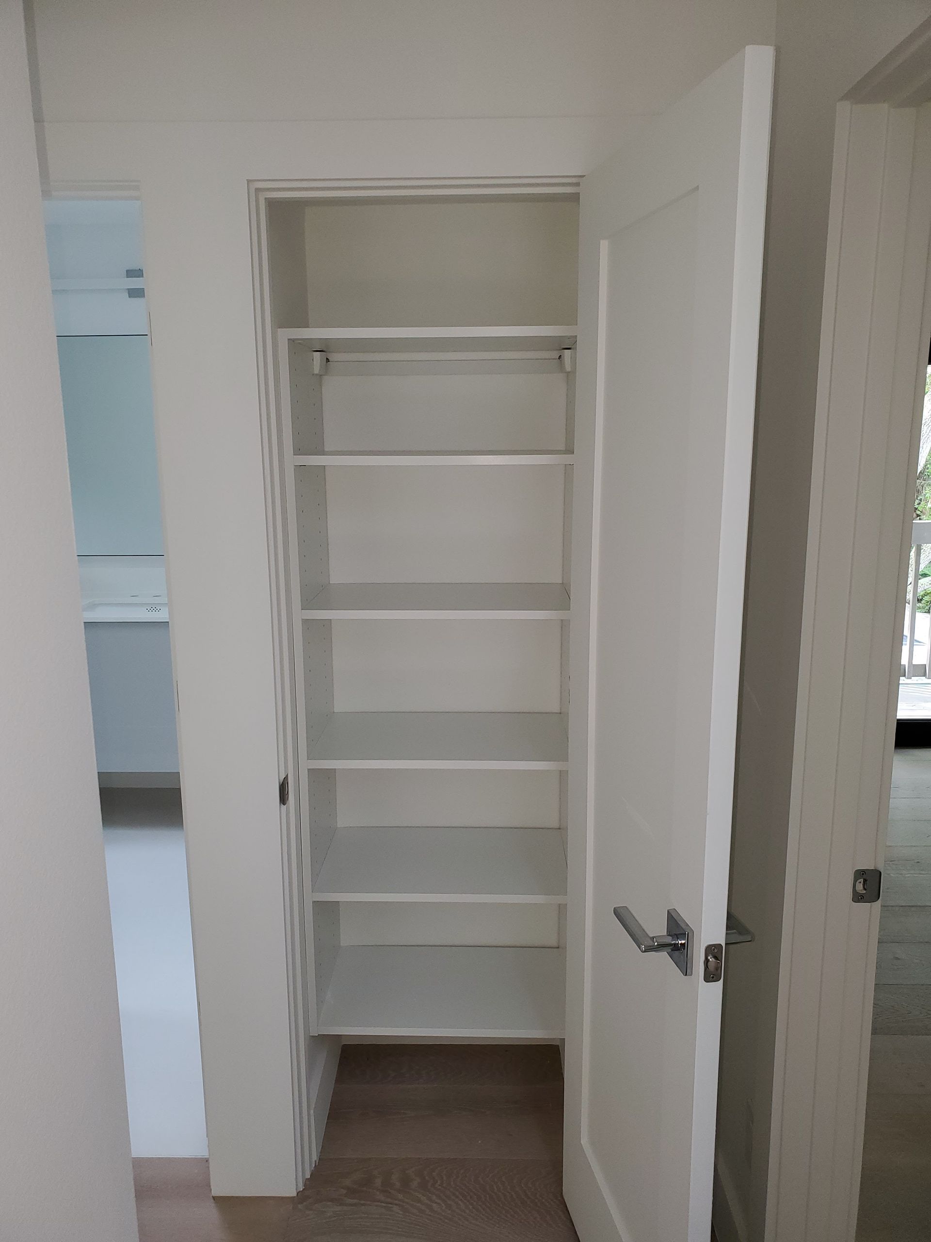 A white, open doorway revealing a narrow pantry closet with six white shelves against a light-colored wall.
